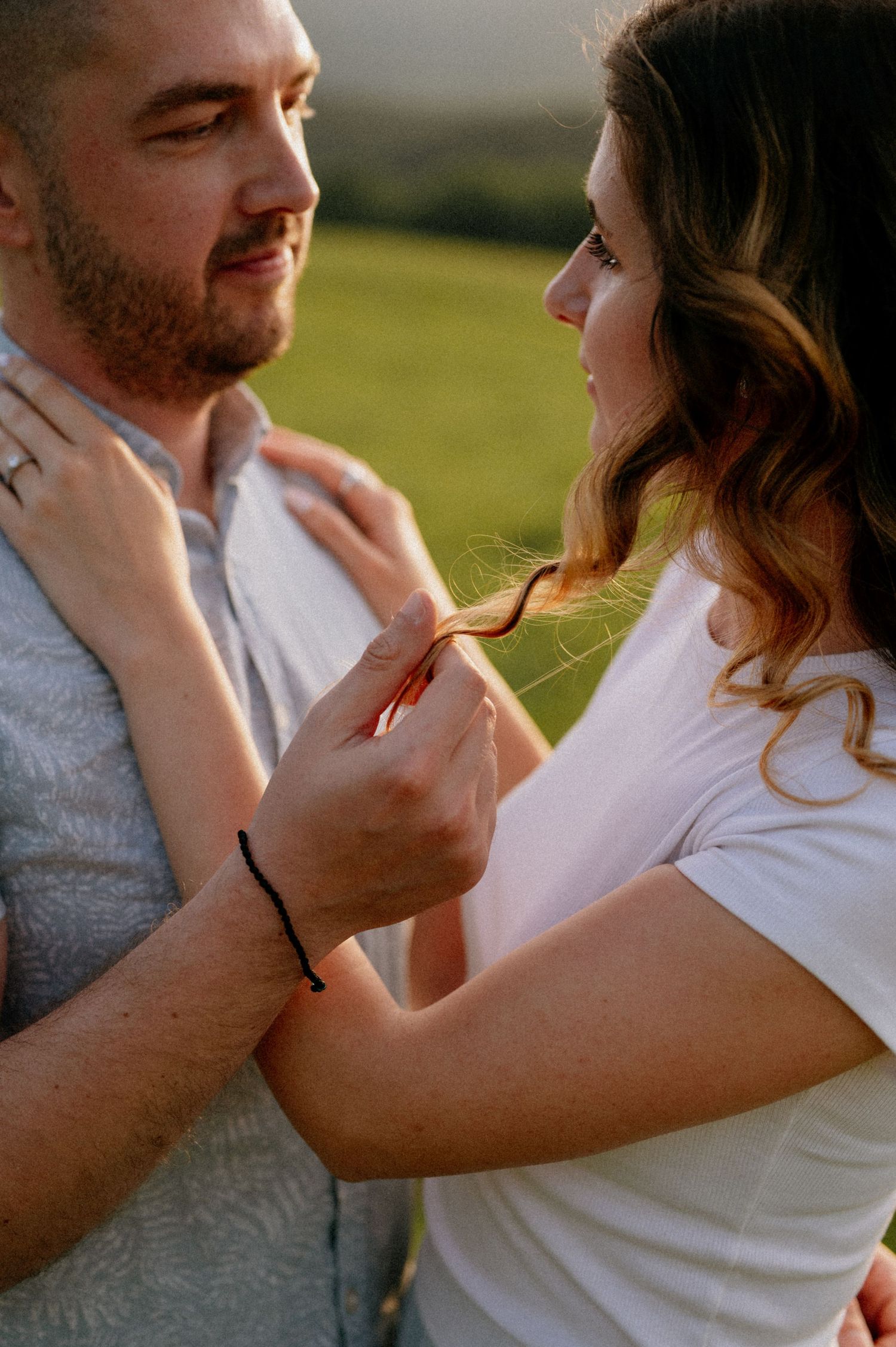 A tender moment between a couple as they gently touch each other's faces against a sunset backdrop.