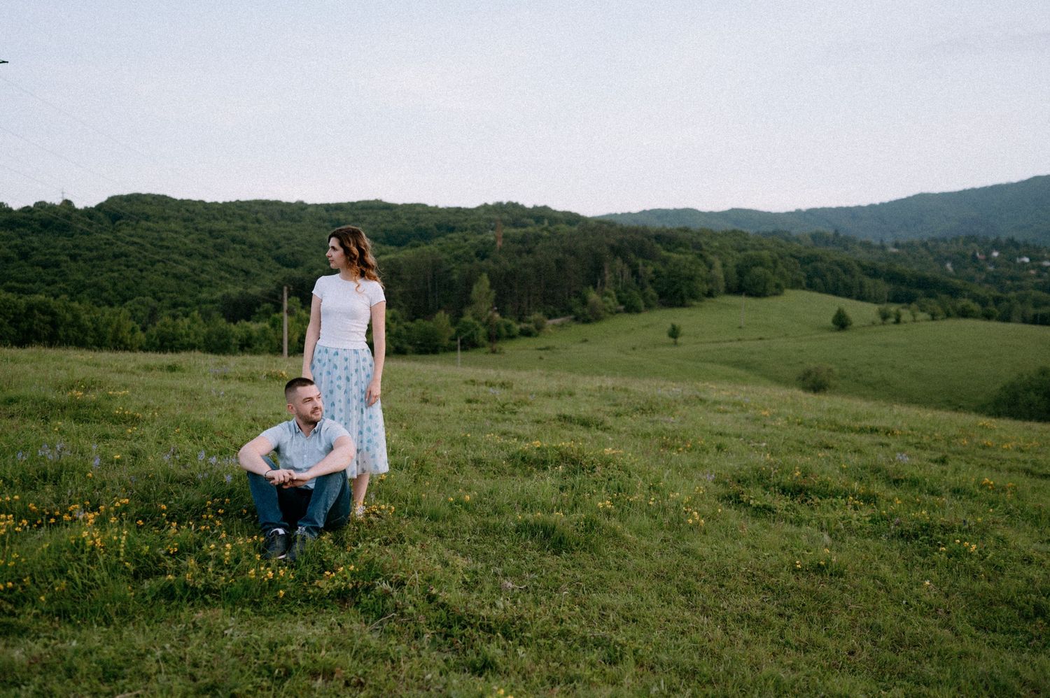 A couple sits together in a scenic mountain field dotted with spring wildflowers.