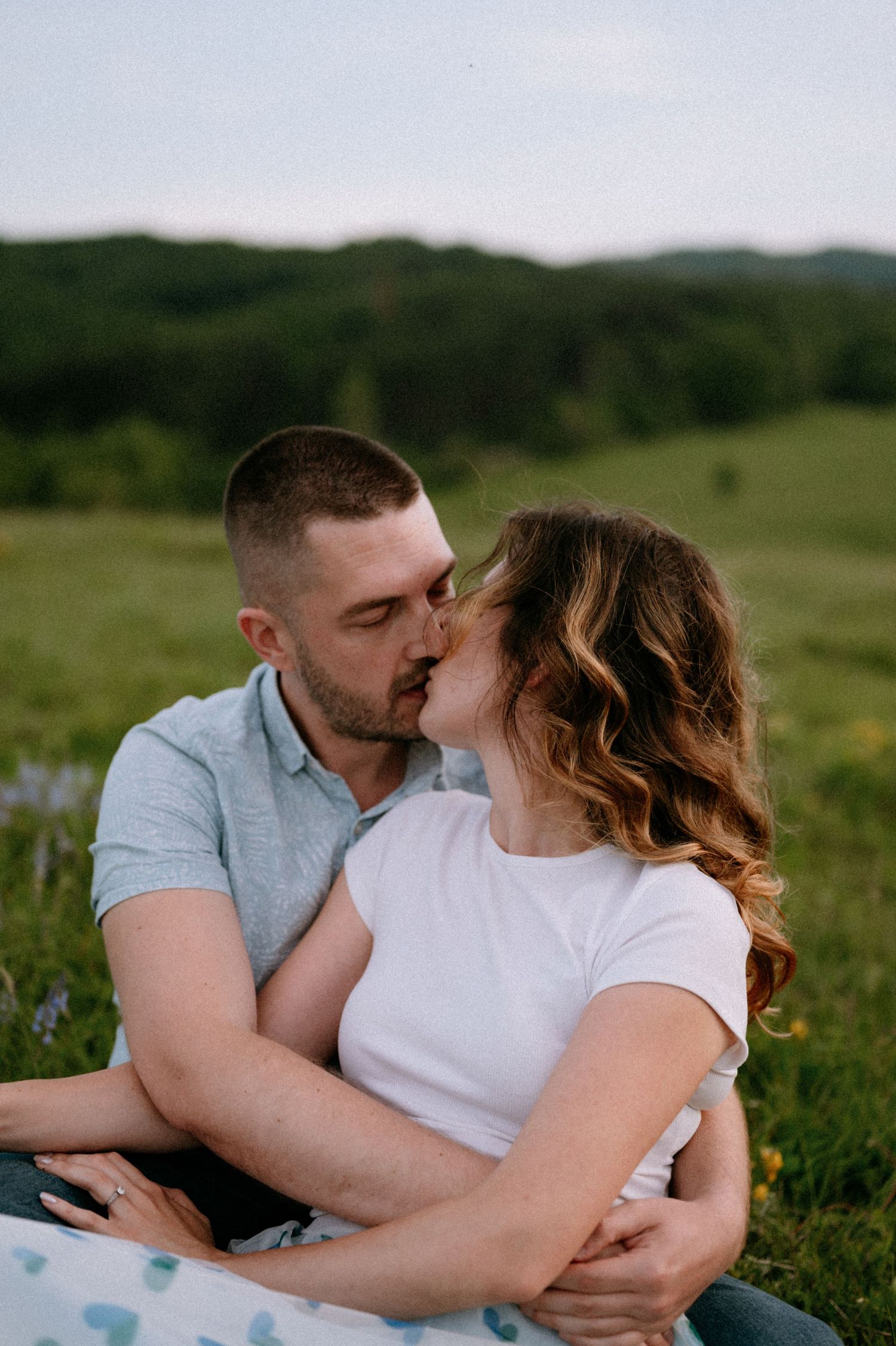 Couple sharing romantic kiss while relaxing in mountain meadow with wildflowers.