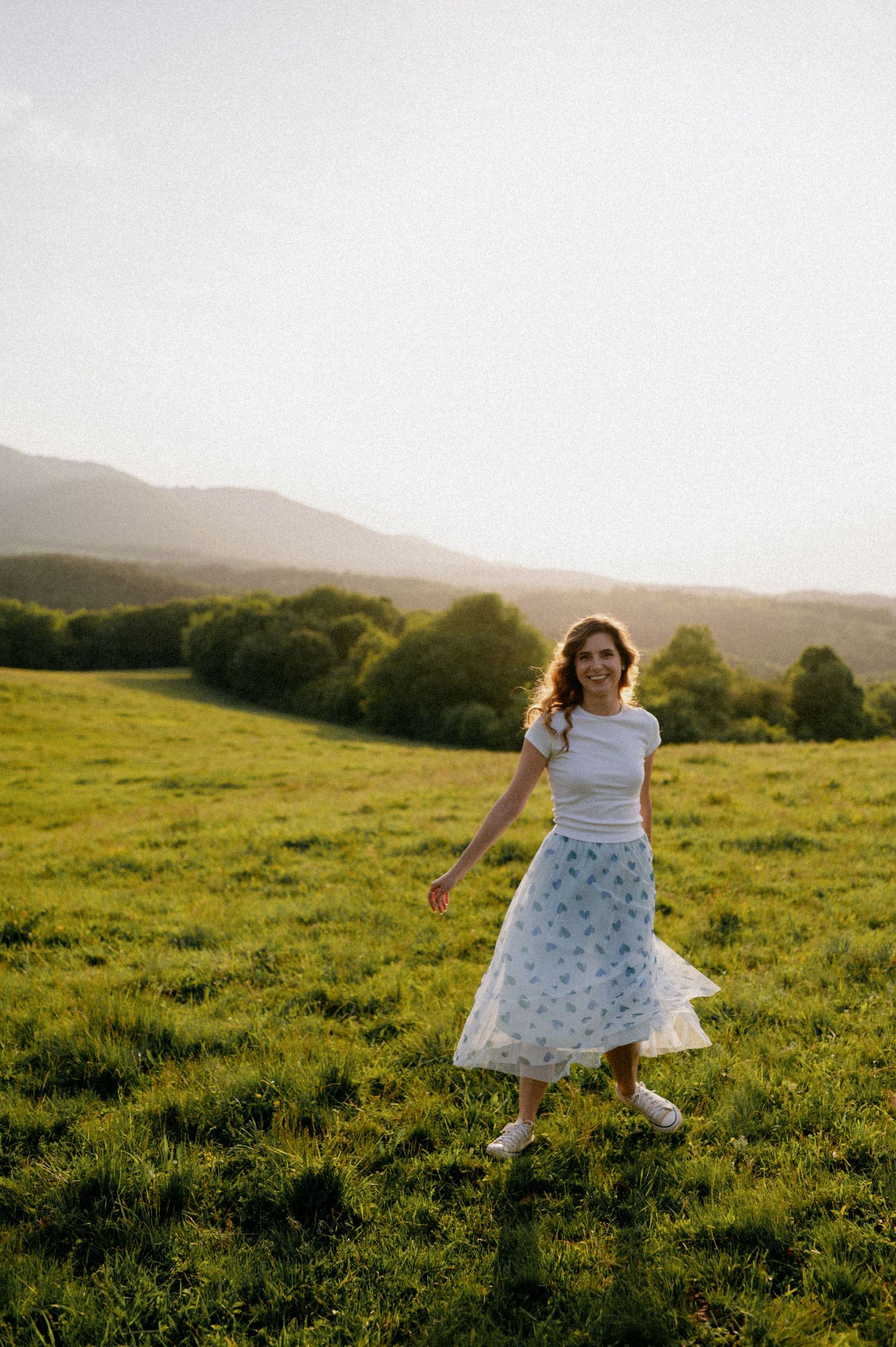 A person in a dotted dress dances carefree across a sunlit mountain meadow.
