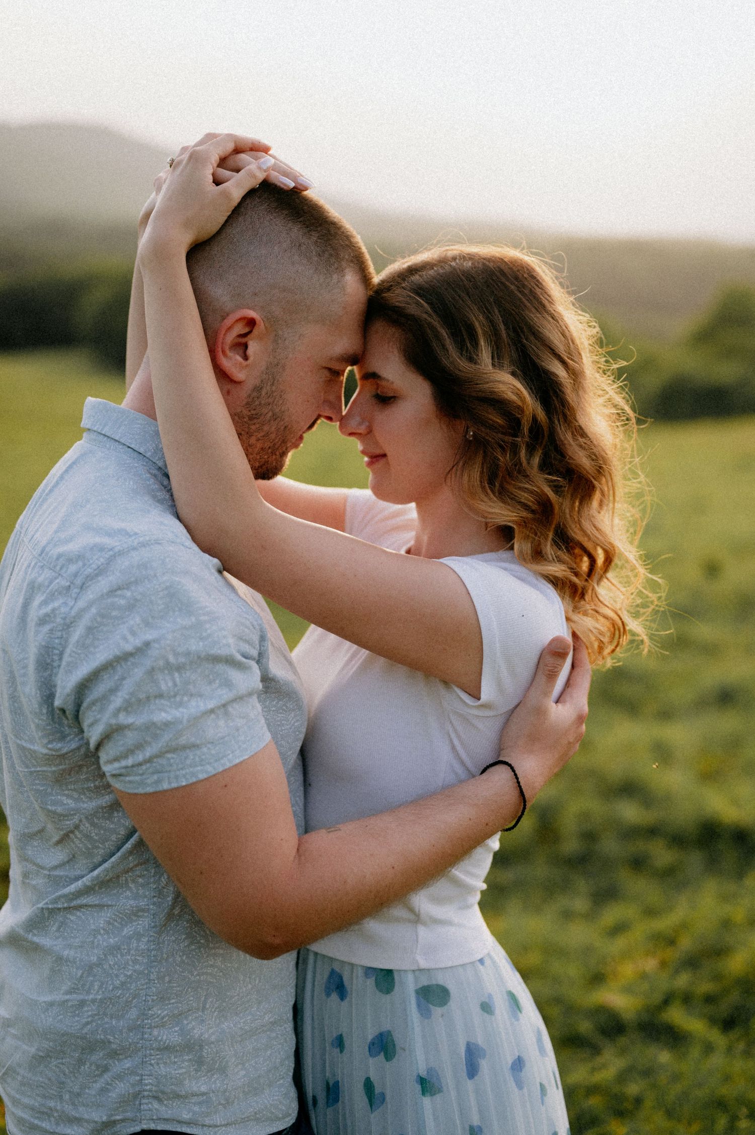 Couple shares tender moment while dancing in nature during sunset photoshoot.