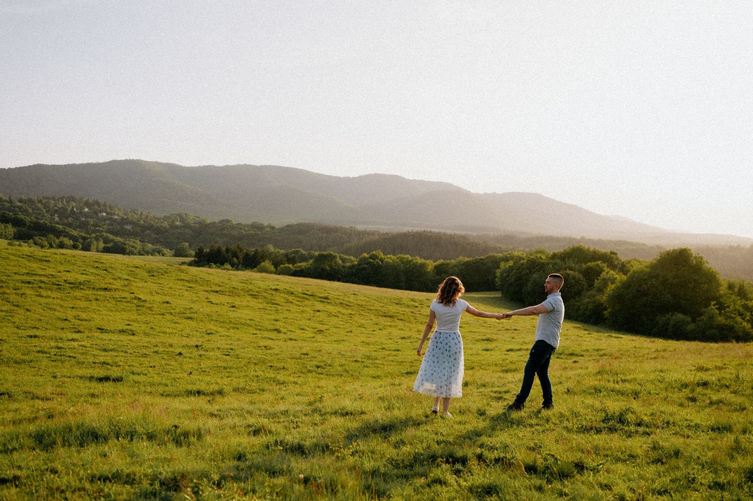 Silhouettes of a couple walking through a sunlit meadow with mountain views.