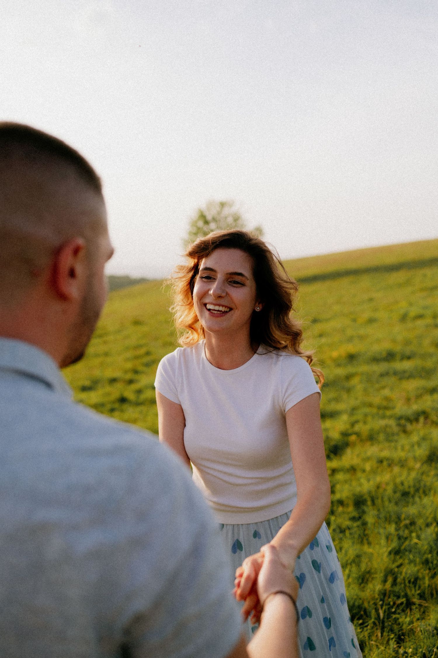 Two people share a playful moment while dancing in a sunlit field.