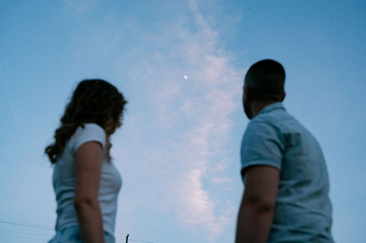 Two silhouettes stand against a dreamy blue sky at dusk.