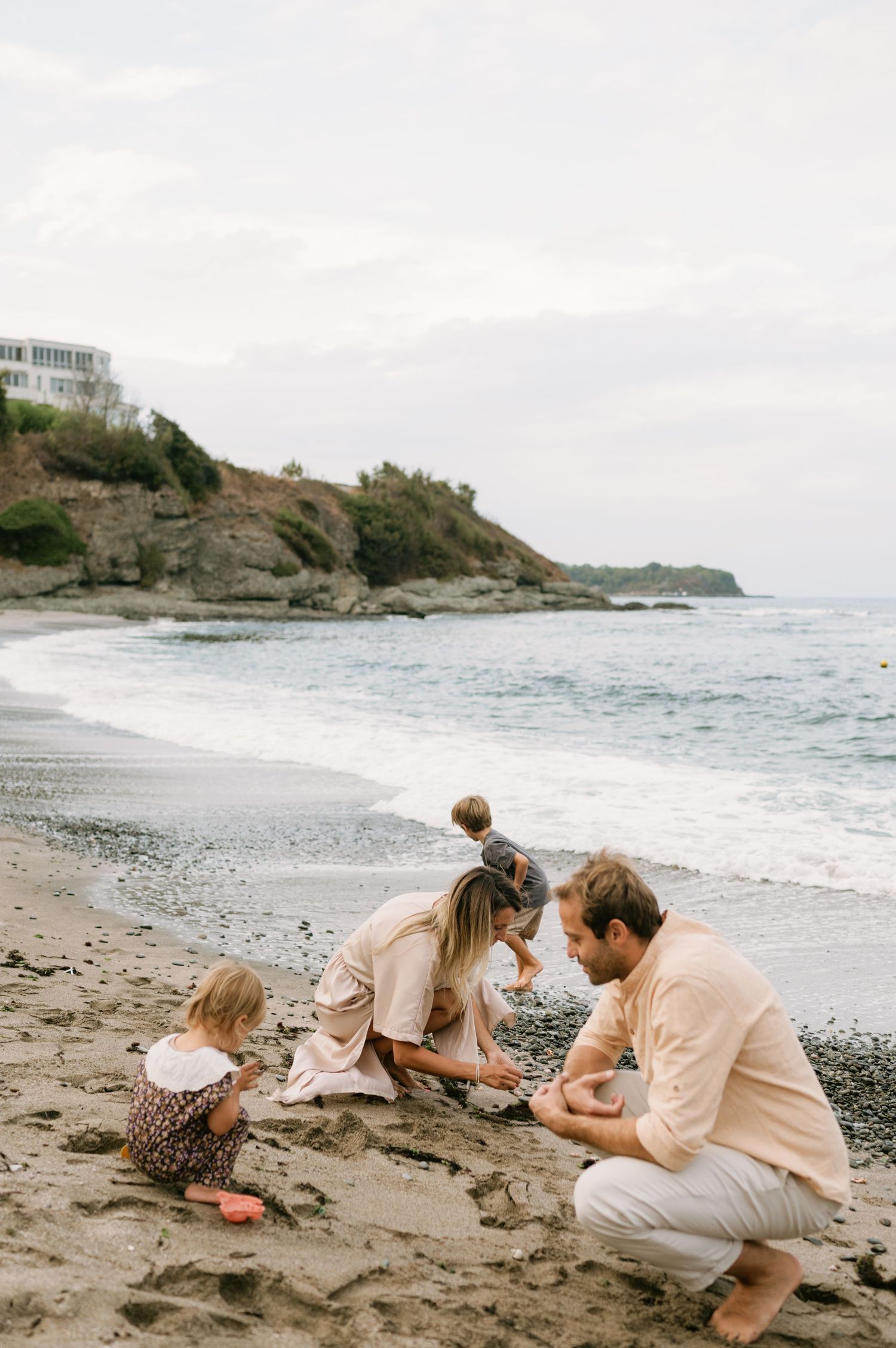Family playing together on a sandy beach shore with rocky cliffs and ocean waves in the background.