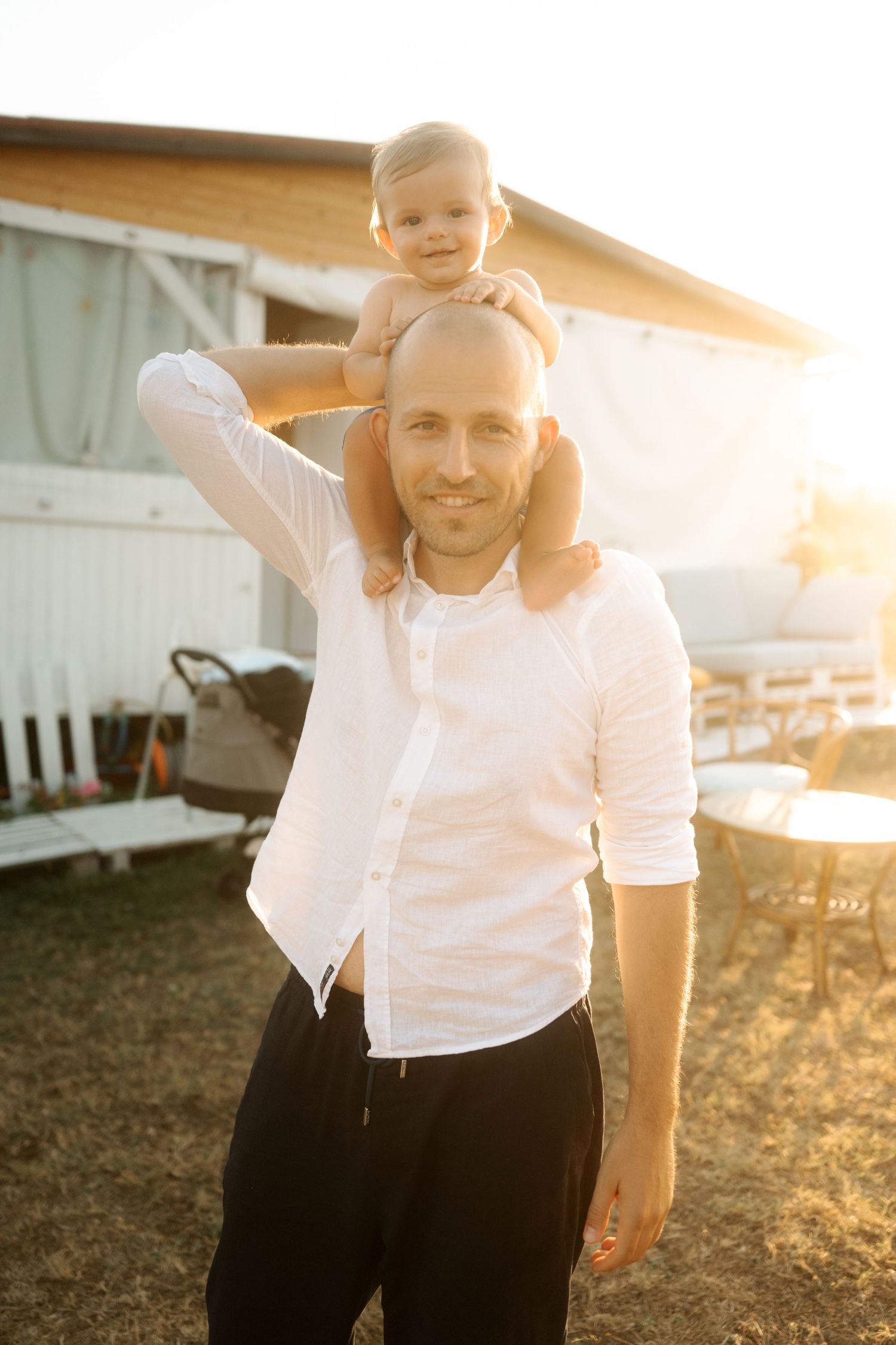 A warm sunset photo of a parent and child outdoors near a white building on a summer evening.