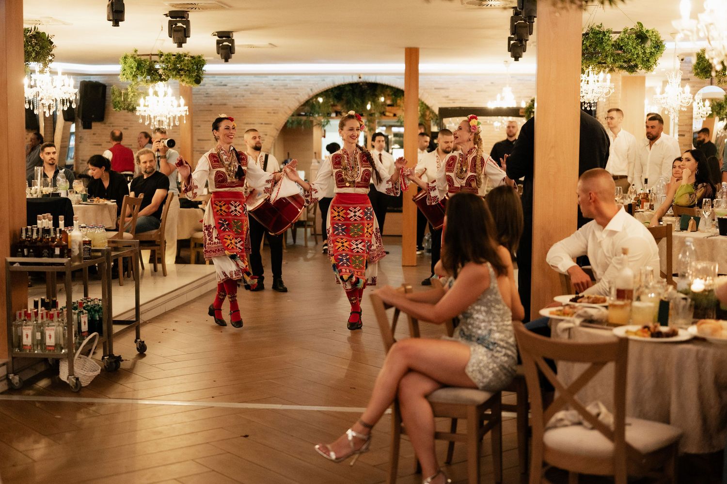 Wedding reception venue decorated with hanging grapes and warm lighting showcases elegant table settings and dance floor.