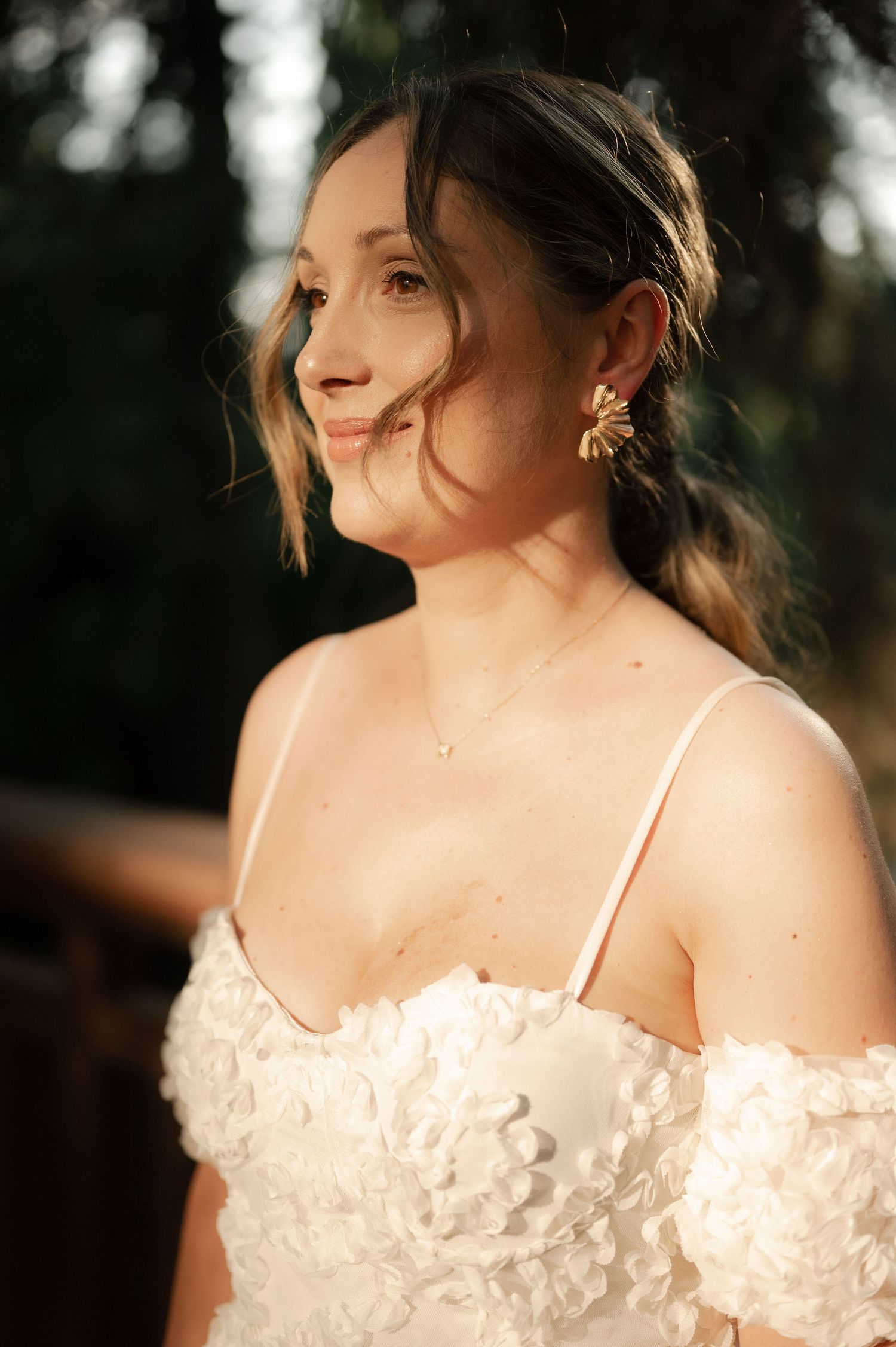 A bride in a white lace off-shoulder wedding dress poses during golden hour sunset photography session.