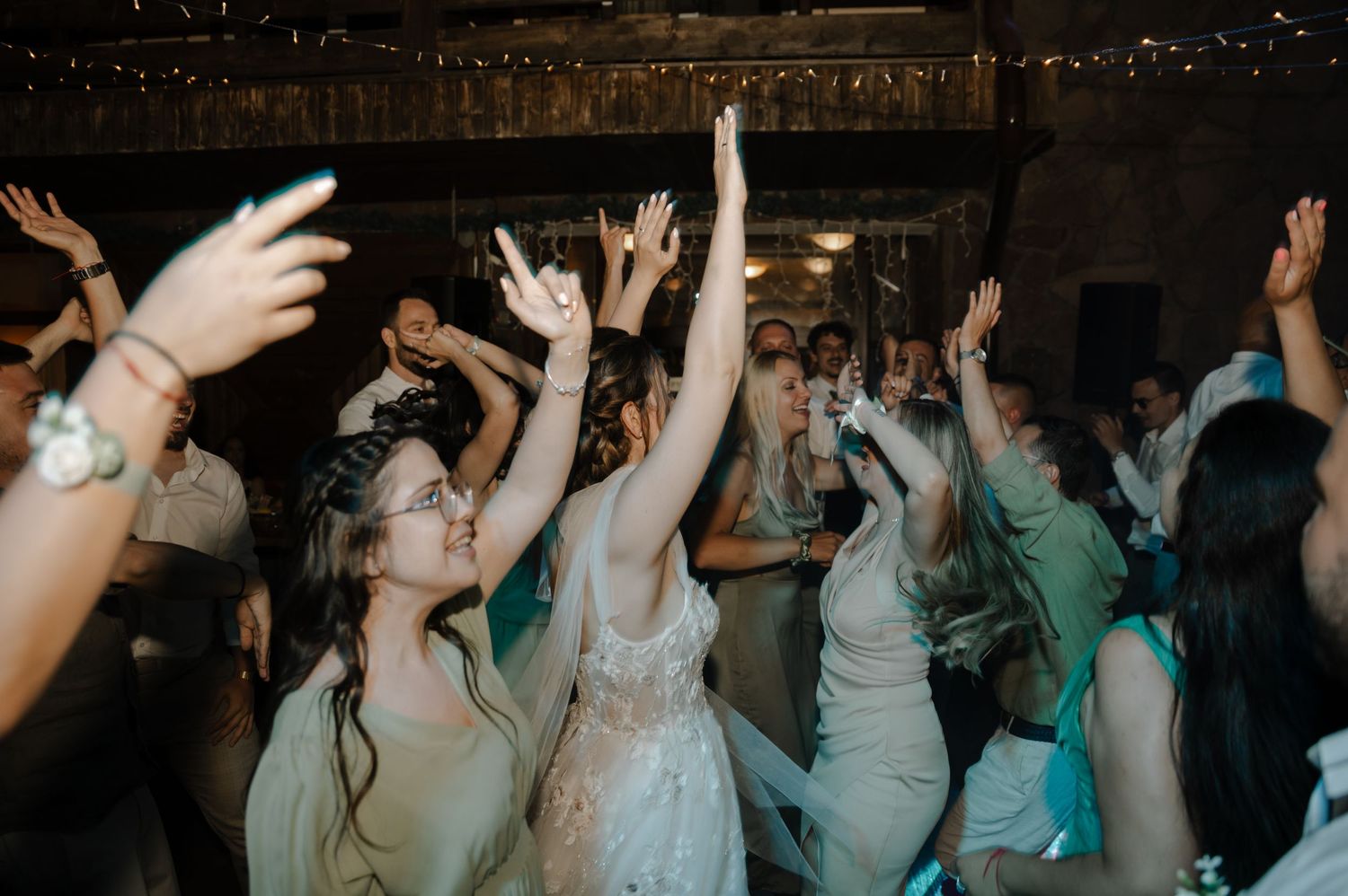 Crowd of party guests with raised arms dancing and celebrating at a dimly lit evening reception.