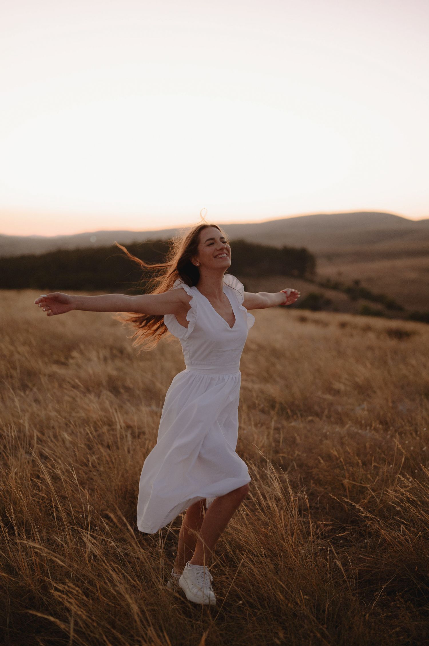 A figure in a flowing white dress dances joyfully through a golden field at sunset.
