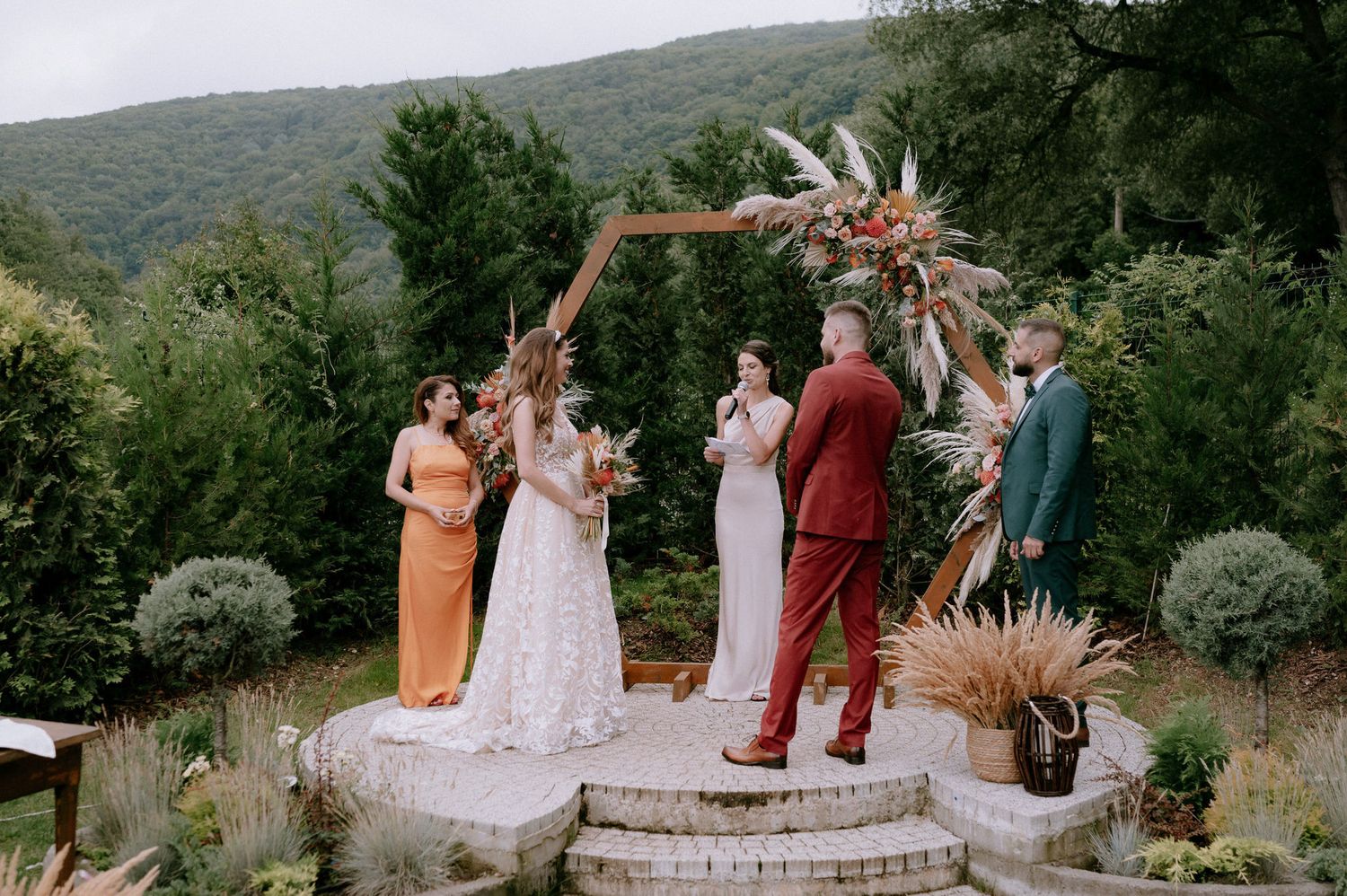 Wedding ceremony taking place on a stone platform surrounded by mountains and greenery in a natural setting.