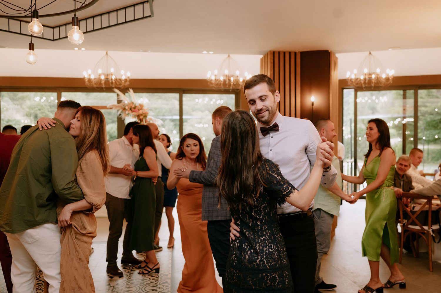 Guests dancing and celebrating at an indoor wedding reception with warm lighting and wood paneled walls.