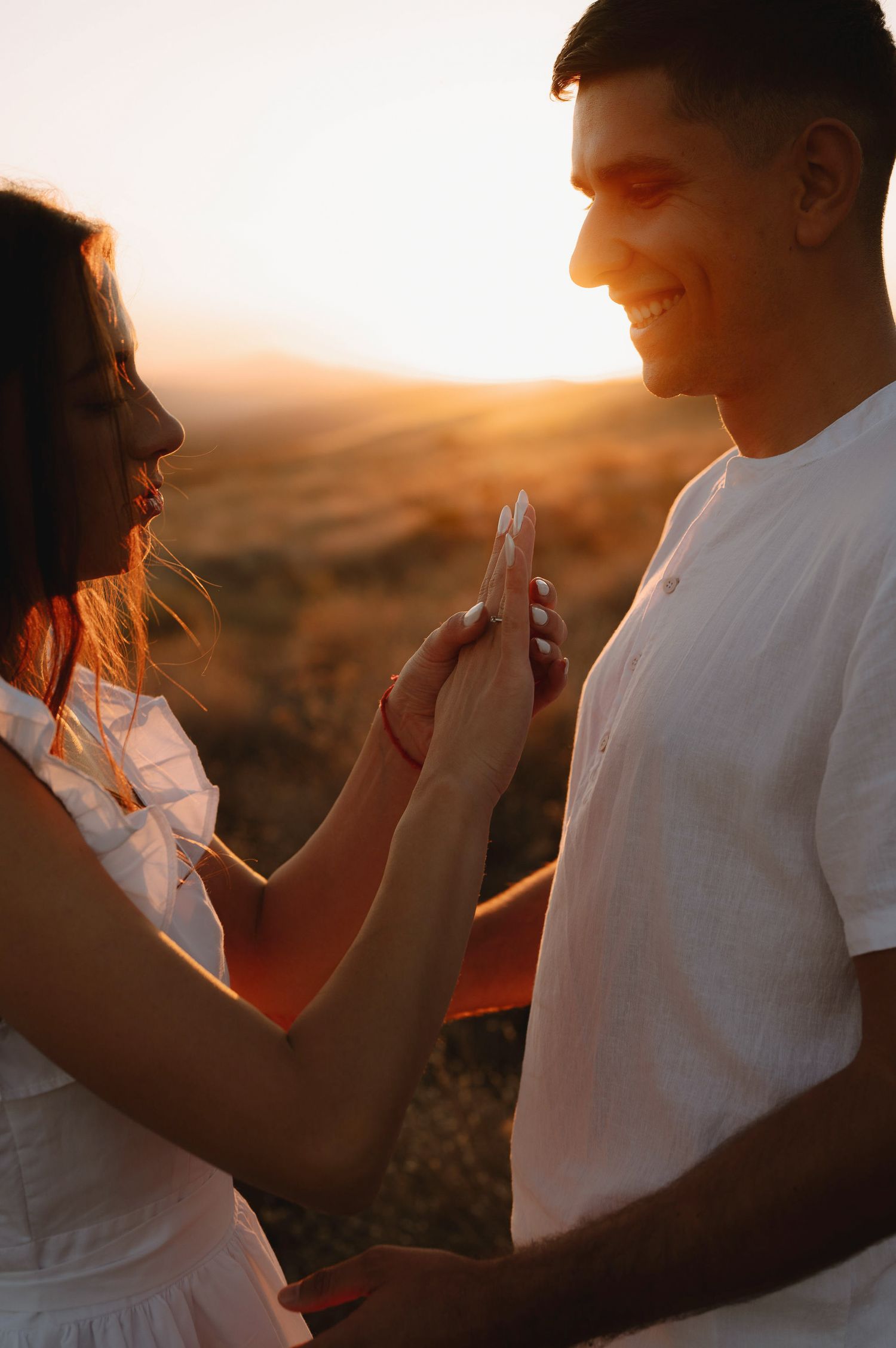 A couple plays patty cake together during golden hour sunset, creating a playful silhouette against warm lighting.
