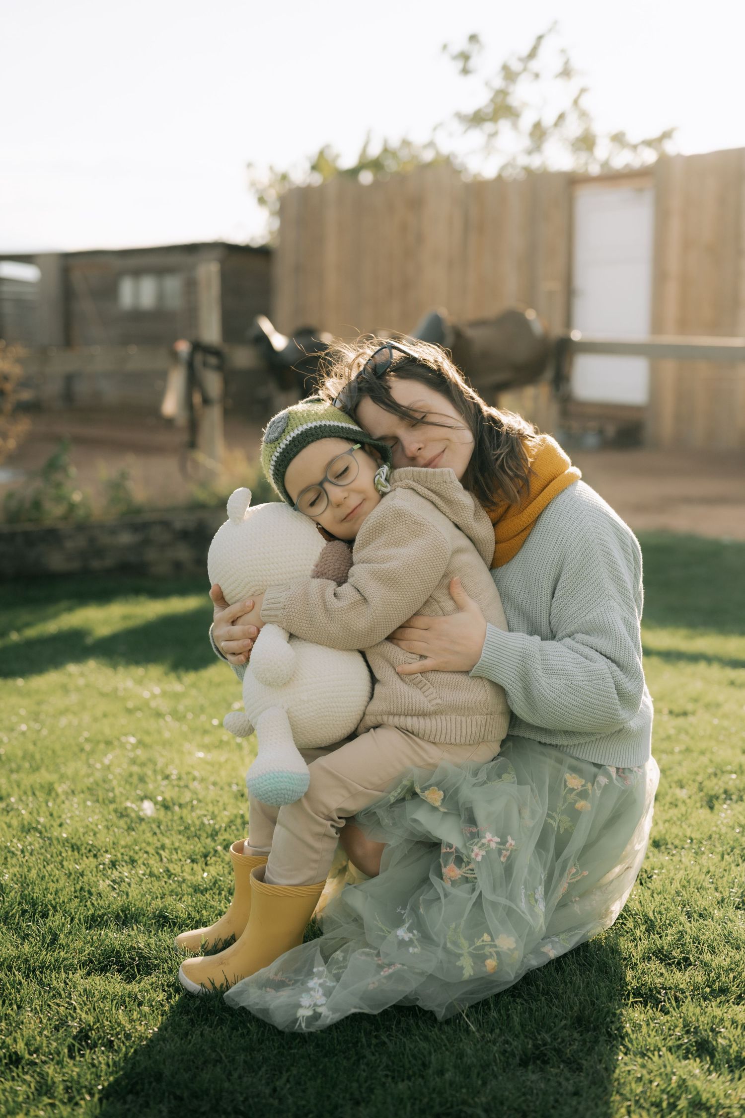 Two people share a tender moment while sitting together on grass during golden hour sunlight.