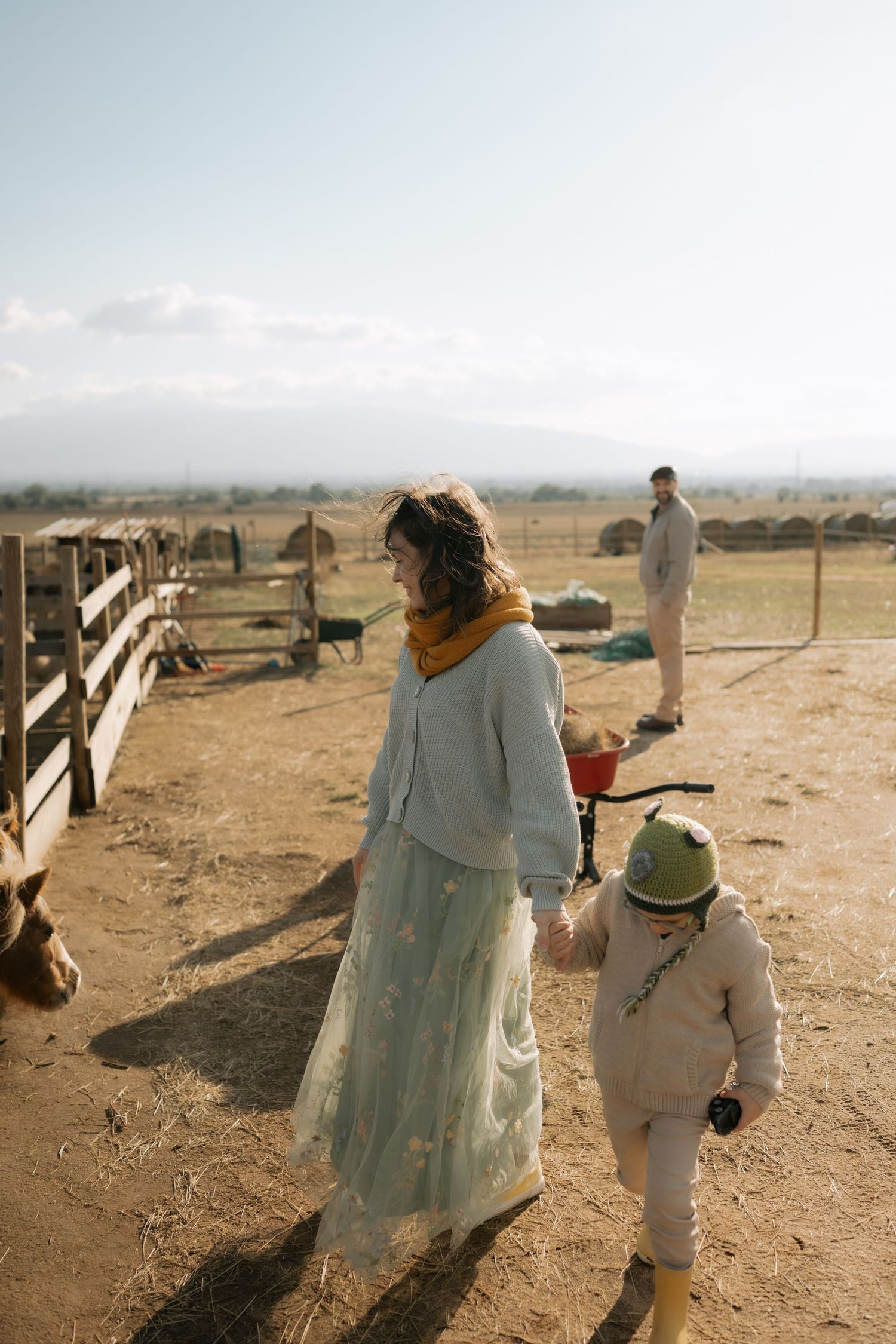 Two people walk together in a desert landscape with wooden fencing visible in the background.