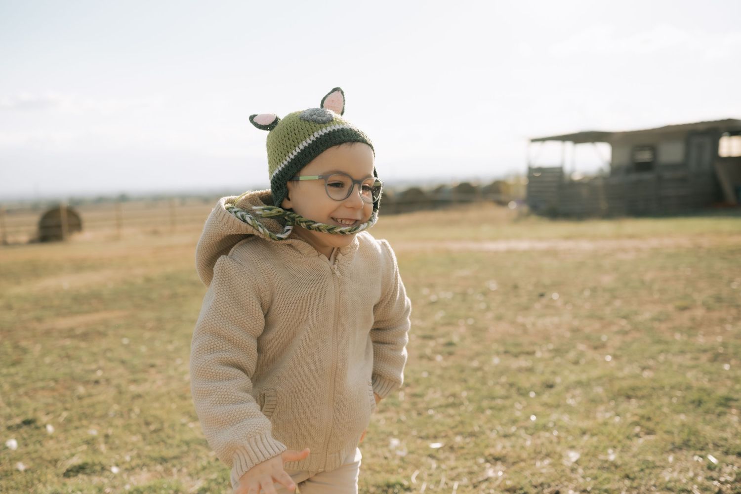 A person in a beige coat and green beanie walks through a golden autumn field on a sunny day.