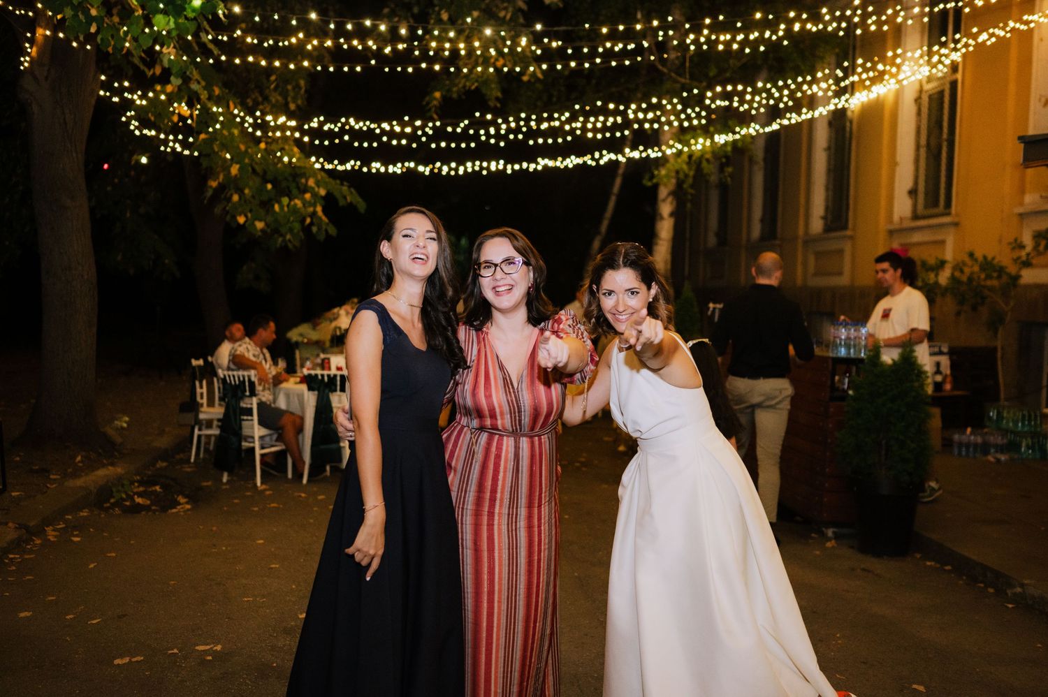 Wedding guests dance and celebrate under twinkling string lights at an outdoor evening reception.