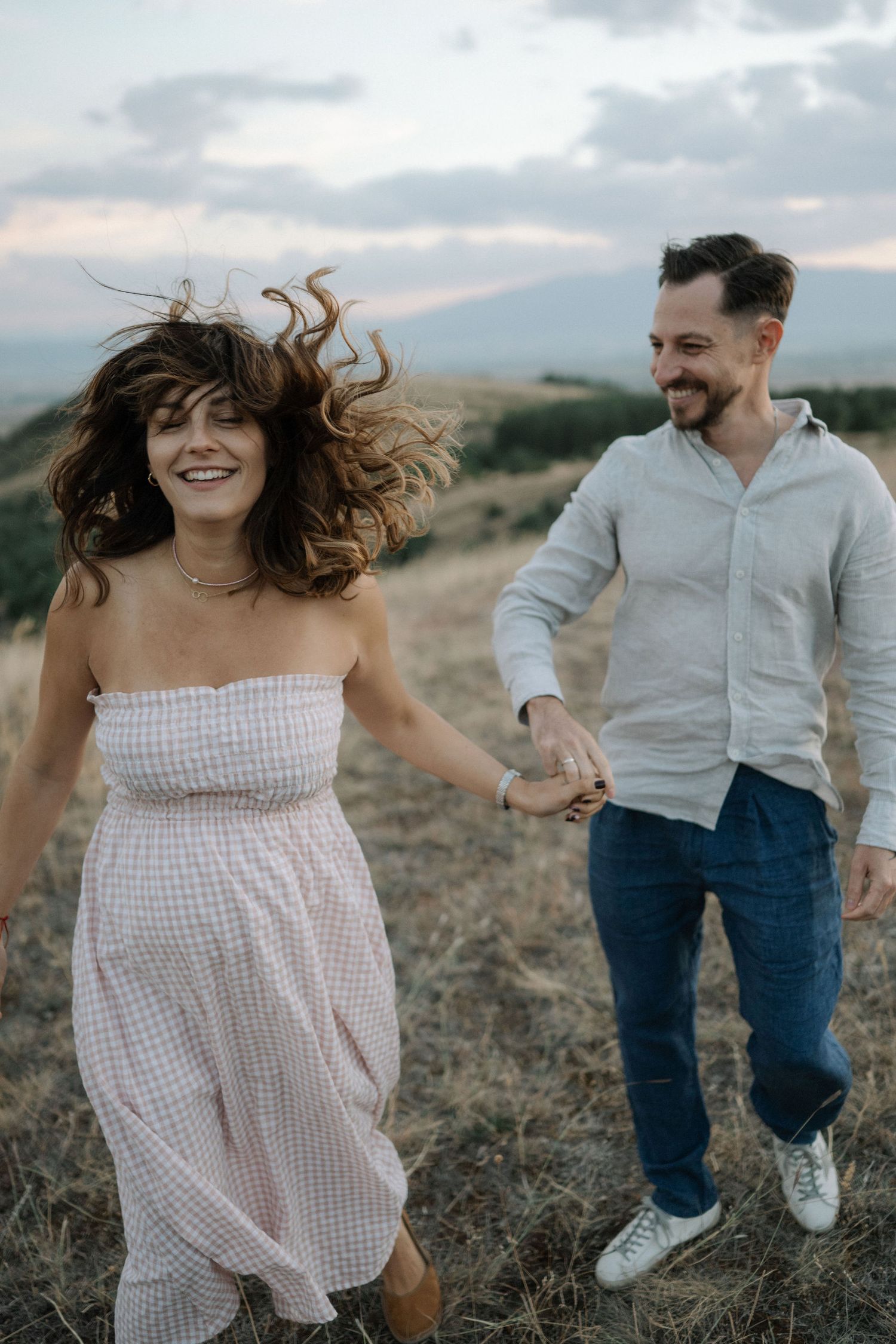 Candid moments of dancing and laughter in a golden field during sunset.
