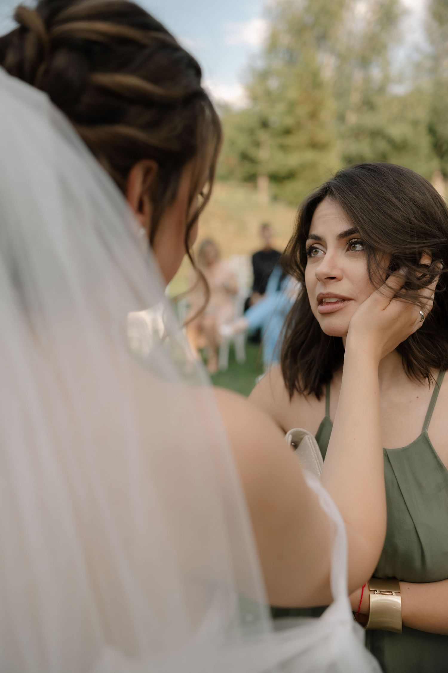 Emotional wedding moment captured as bride and bridesmaids share tears and laughter during outdoor ceremony.