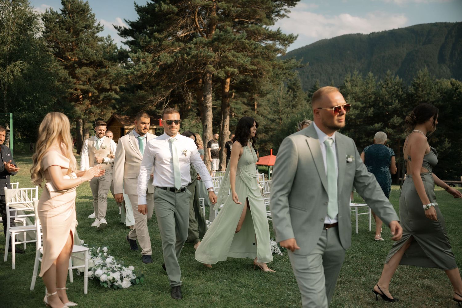 Wedding party members gather on a scenic mountain lawn during a summer celebration.