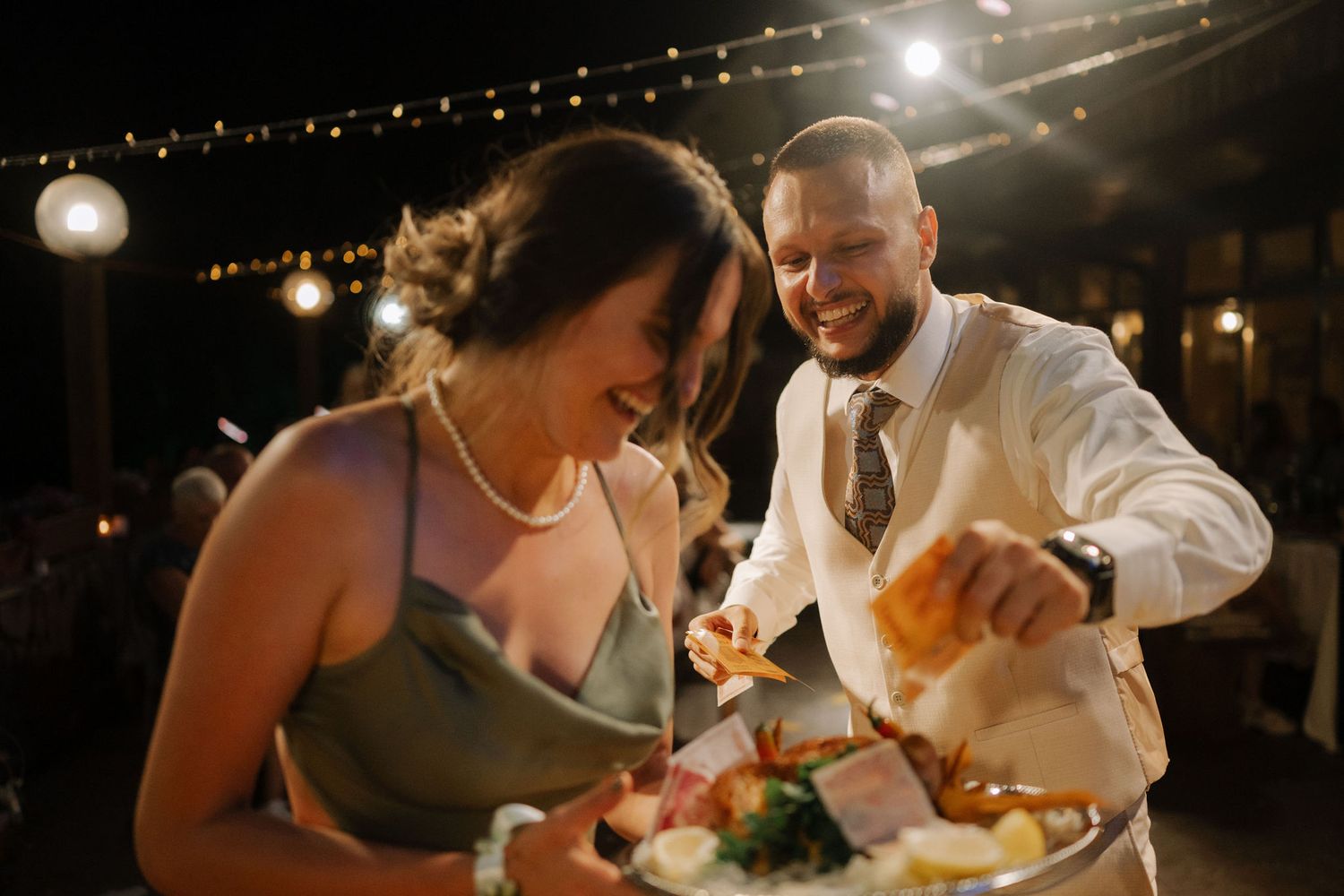 Guests share laughs and conversations during an elegant evening wedding reception under twinkling lights.