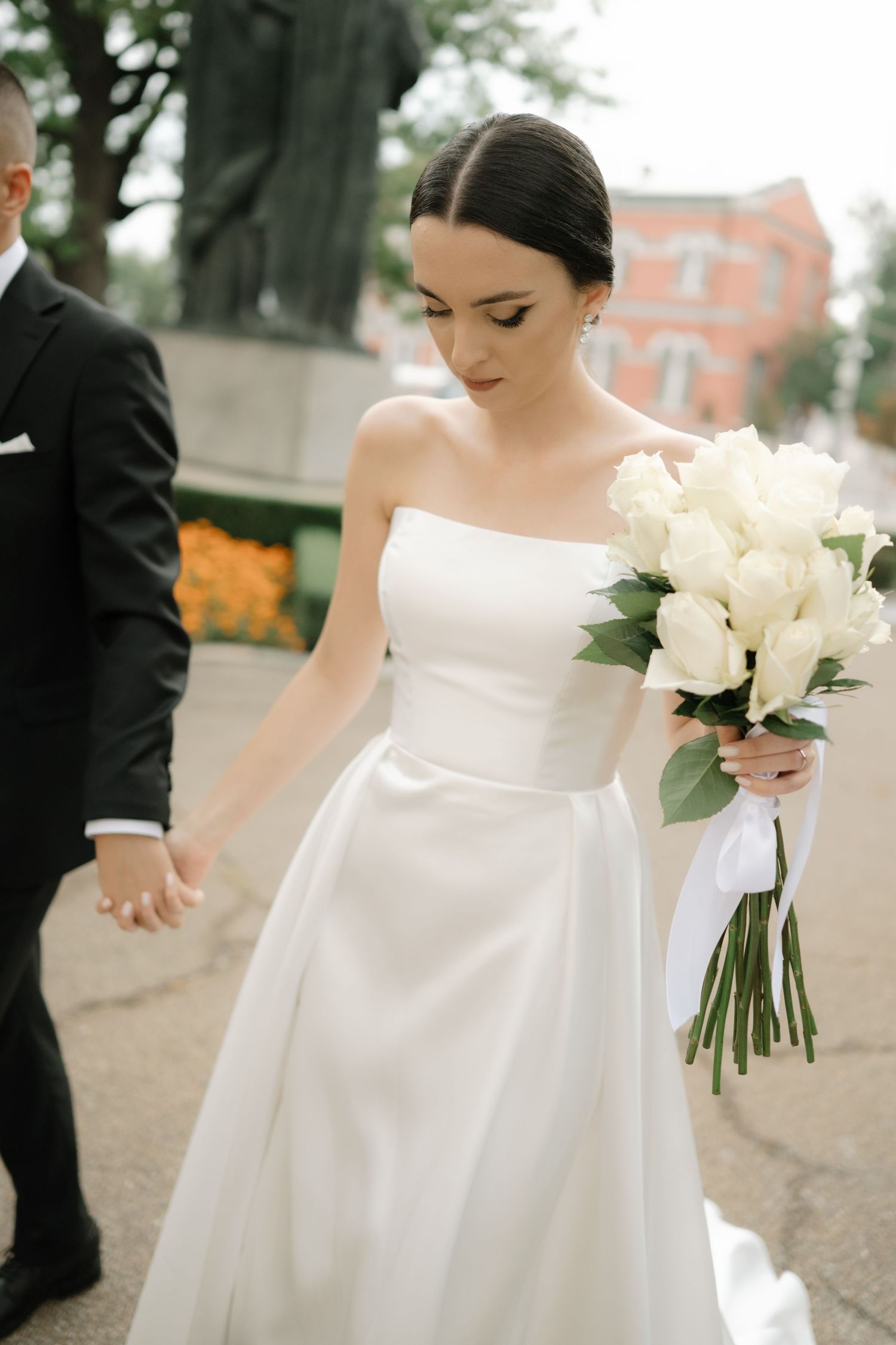 A bride in a classic white strapless wedding gown holds an elegant bouquet of white flowers with greenery.