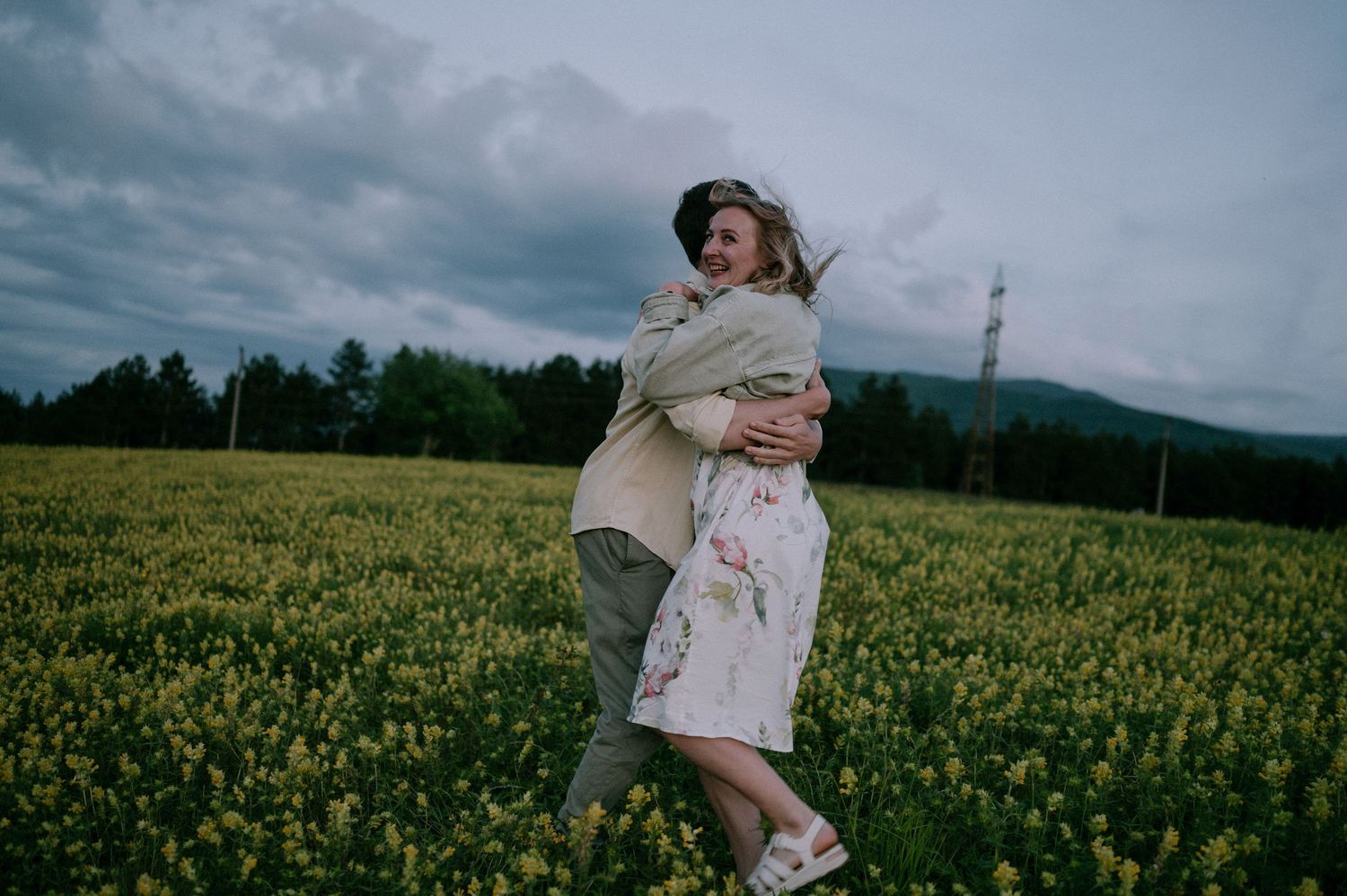 Two people share an intimate embrace while standing in a field of yellow wildflowers.