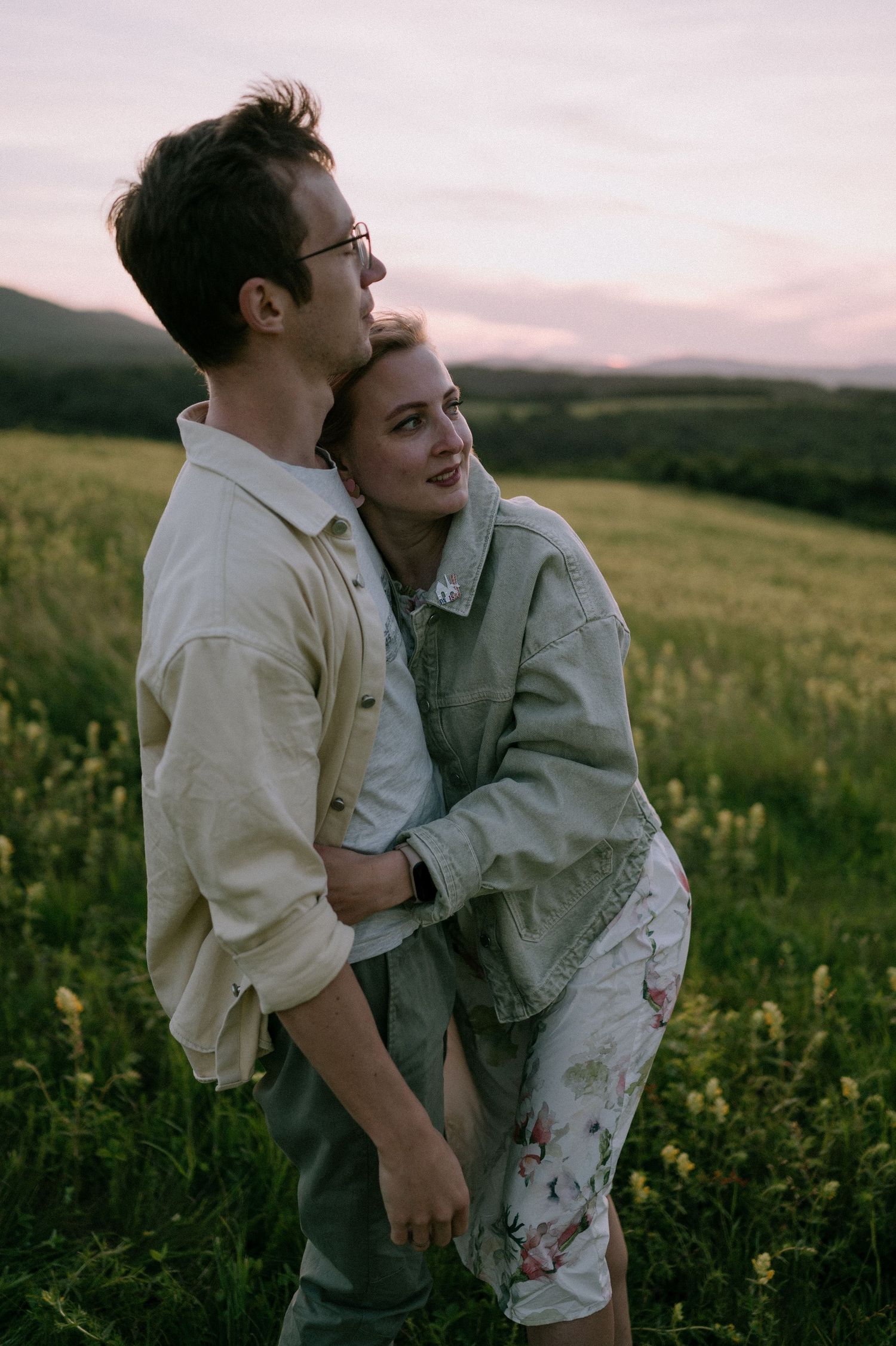 A romantic moment captured between two people embracing in a flowering meadow during sunset.