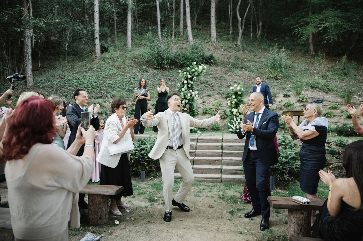 Wedding guests seated on wooden benches in a natural forest amphitheater setting.