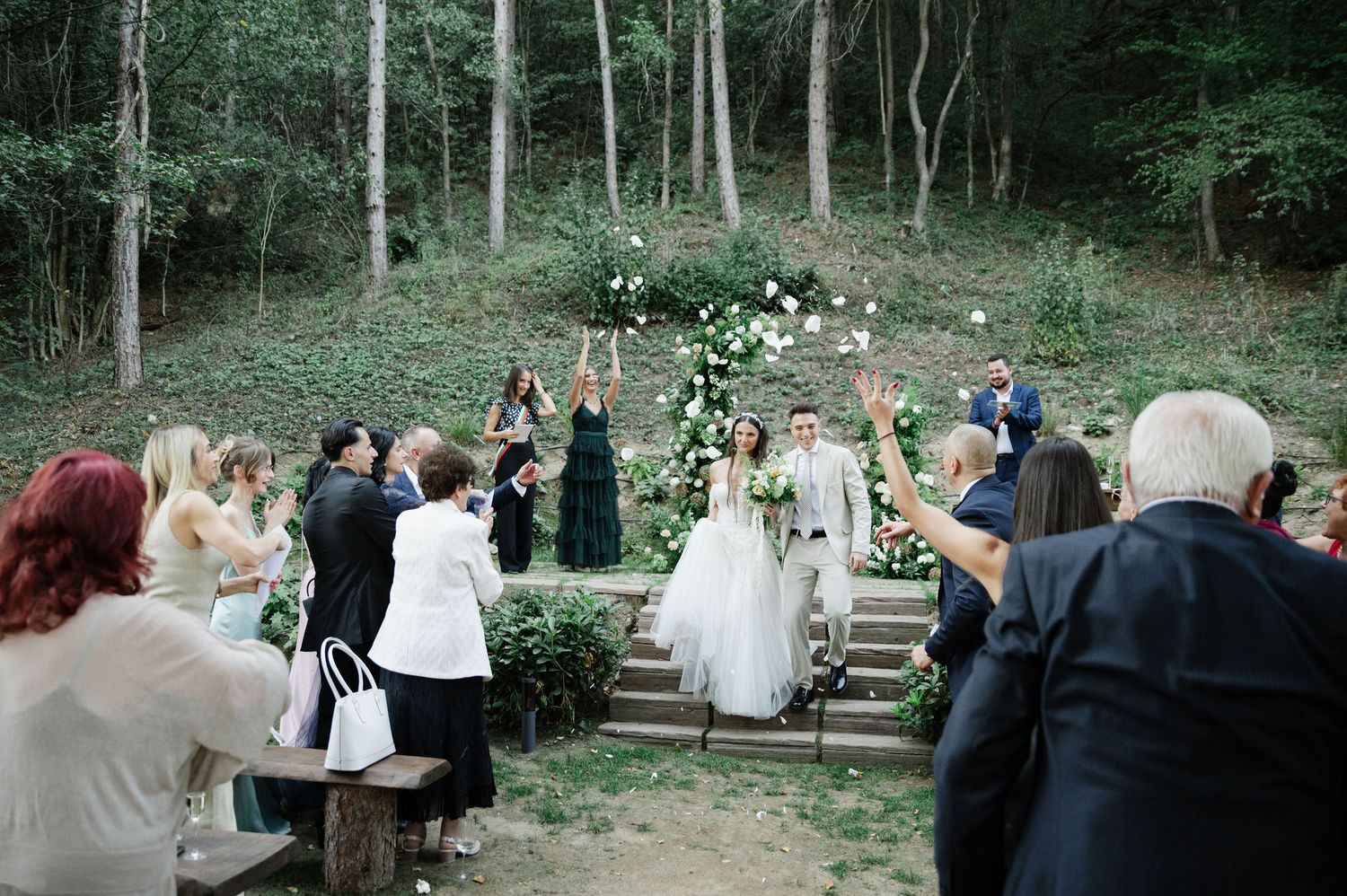Outdoor wedding ceremony space with wooden benches arranged on a hillside among trees.