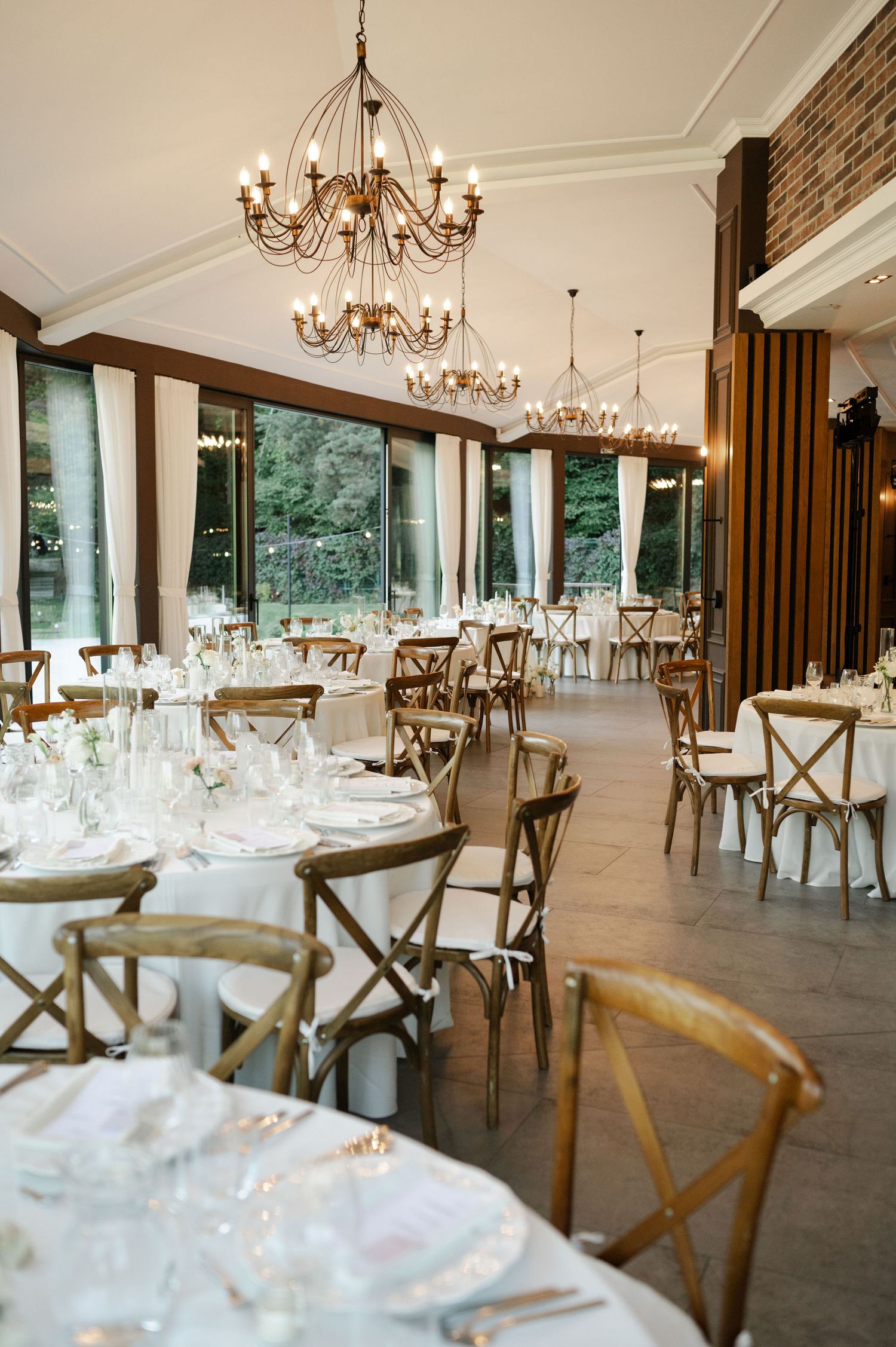 Spacious reception venue with wooden crossback chairs and elegant chandeliers.