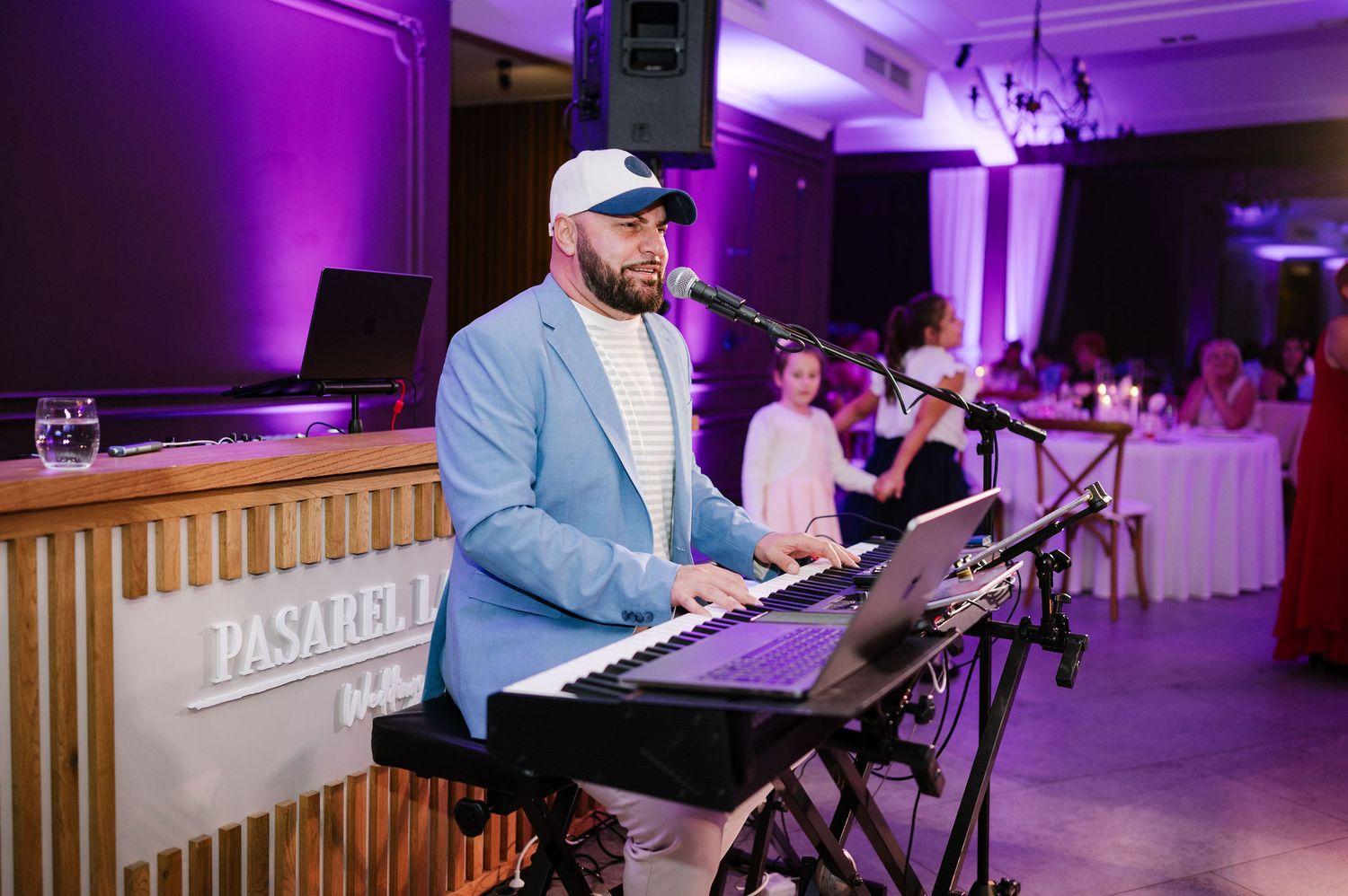 Musician performing at keyboard under purple stage lighting at wedding reception.