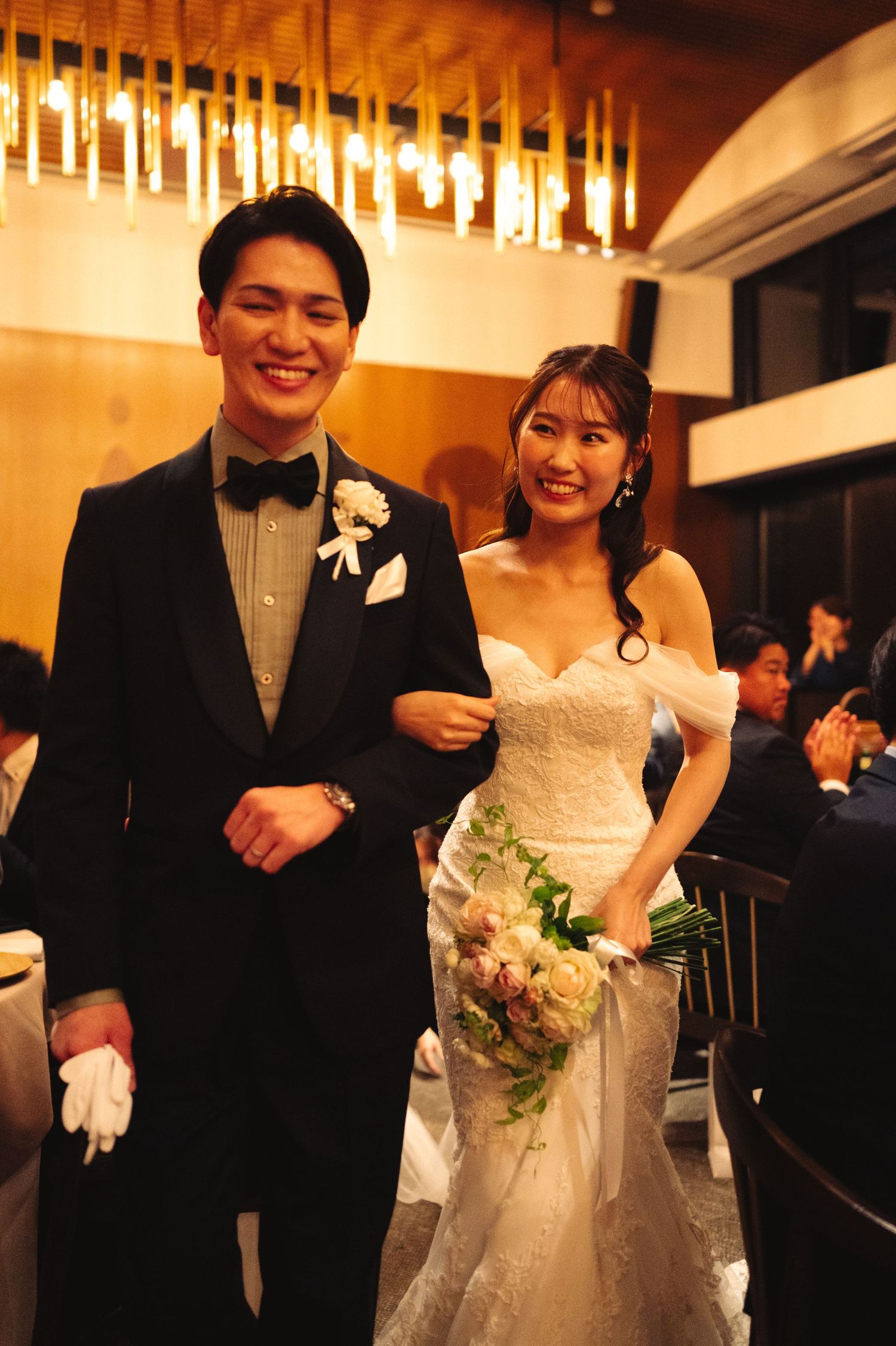Bride in white lace gown and groom in tuxedo celebrate during their wedding reception.