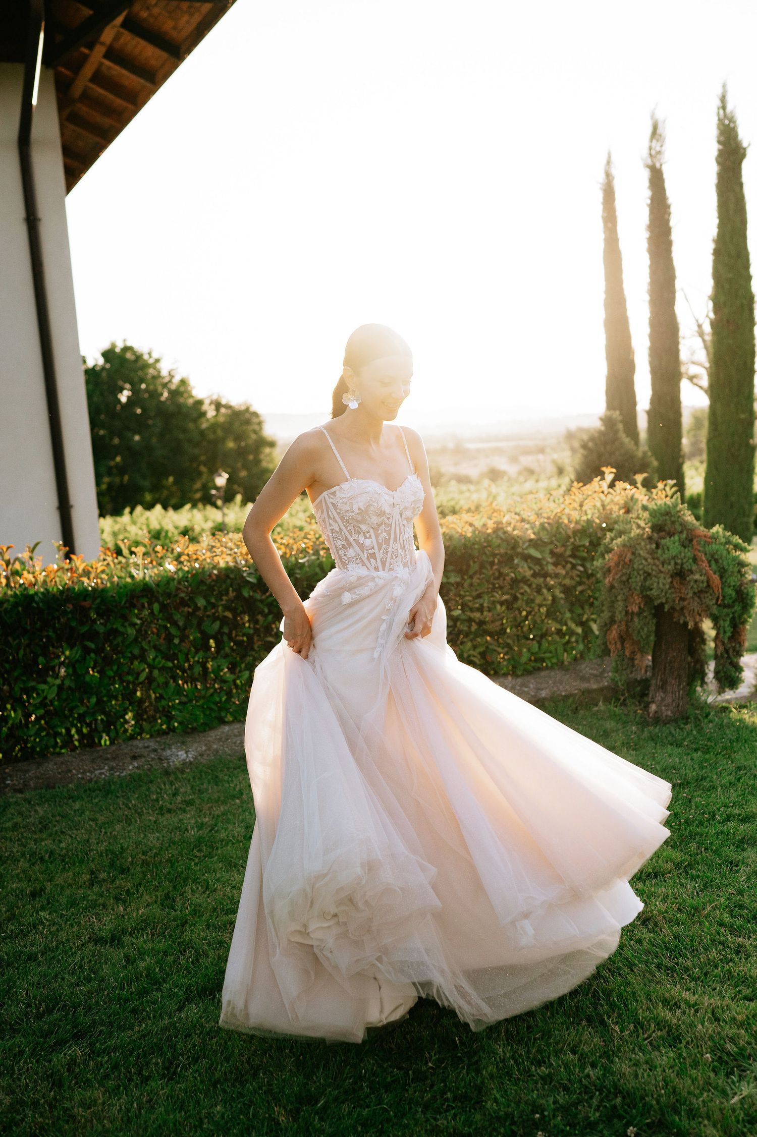 Bride spinning in a voluminous white gown against a backdrop of cypress trees.