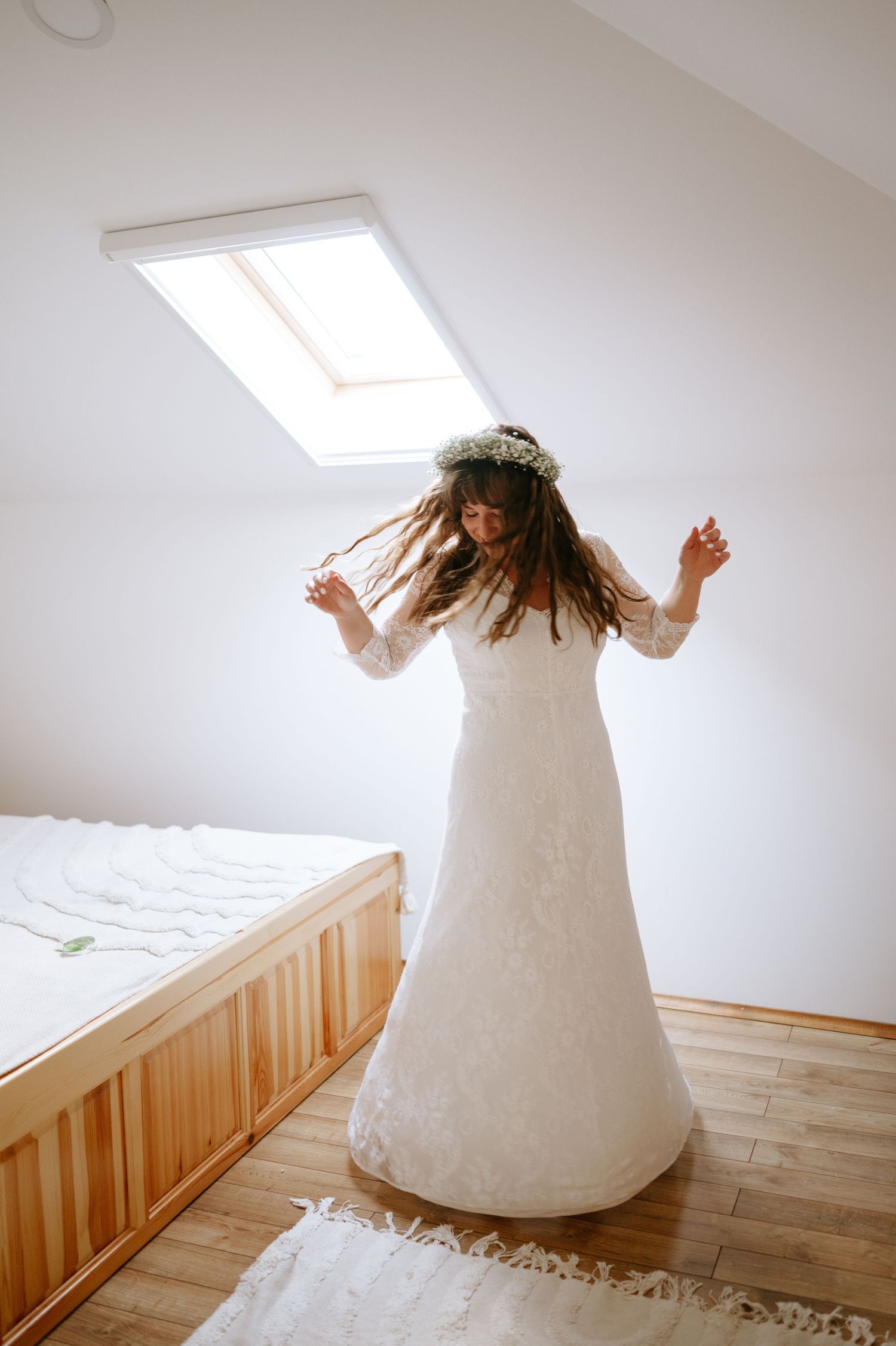 Joyful dancing moment captured in sunlit attic wearing white wedding dress.