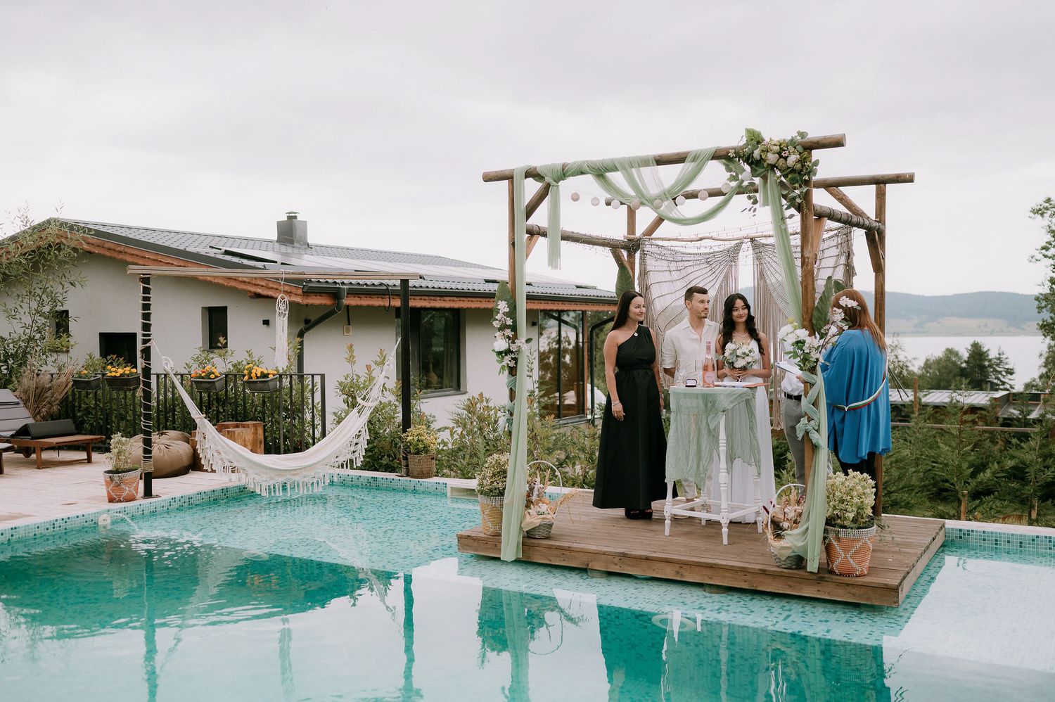 Elegant poolside celebration setup with white decorations and wooden pergola.