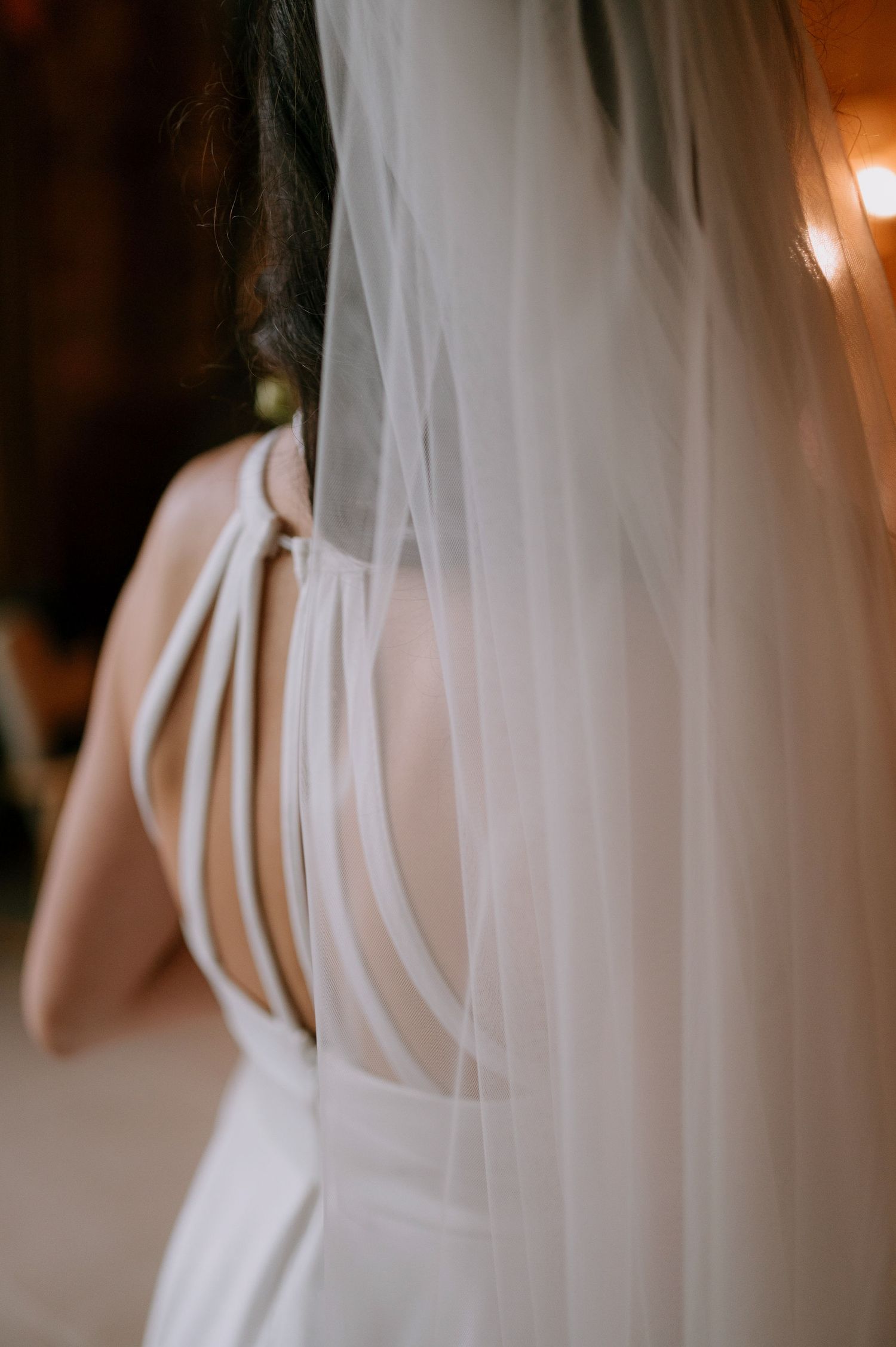 Close-up details of a white wedding dress with delicate straps and veil.