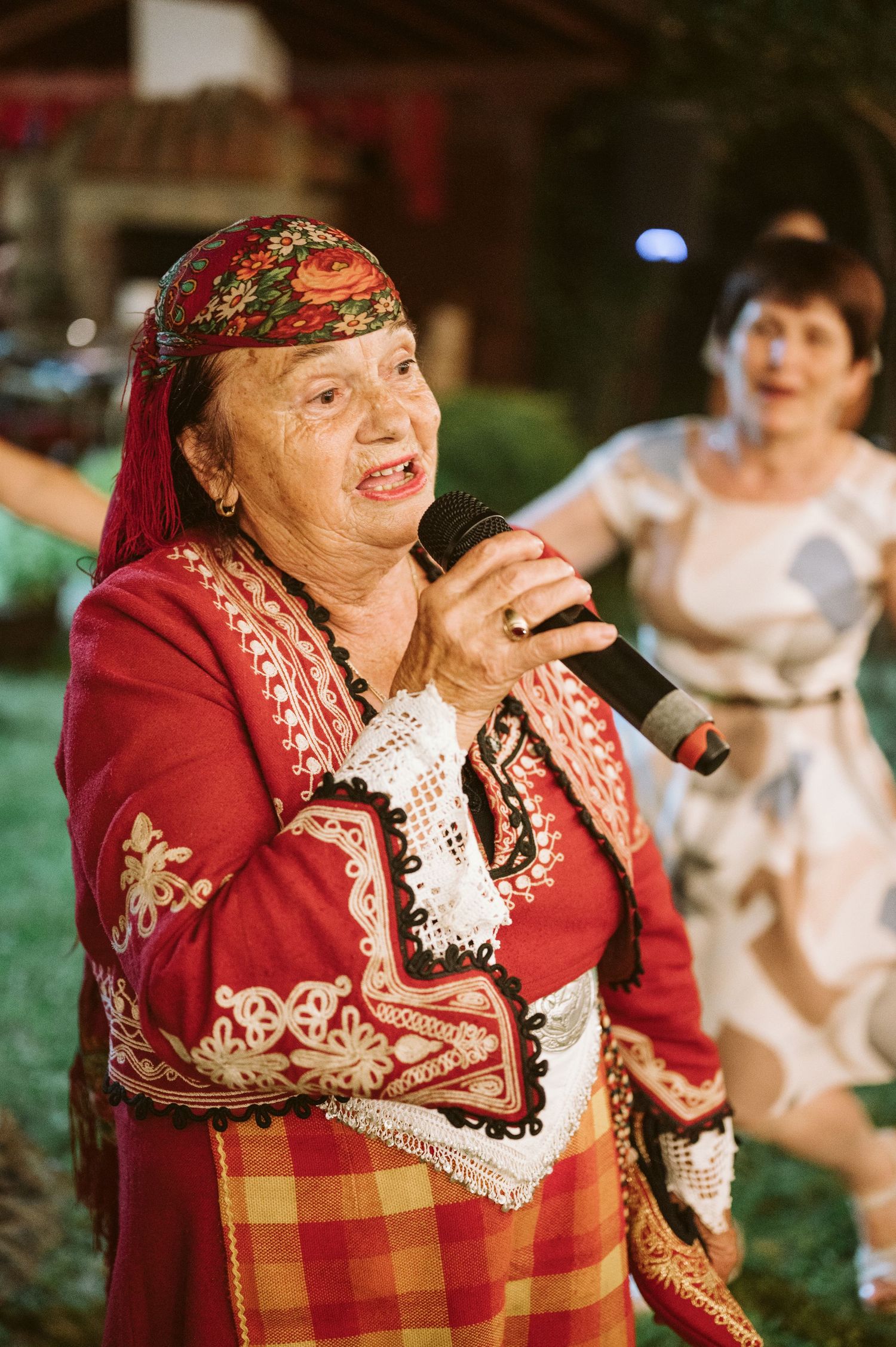 Traditional folk singer in red embroidered dress performs at outdoor wedding.
