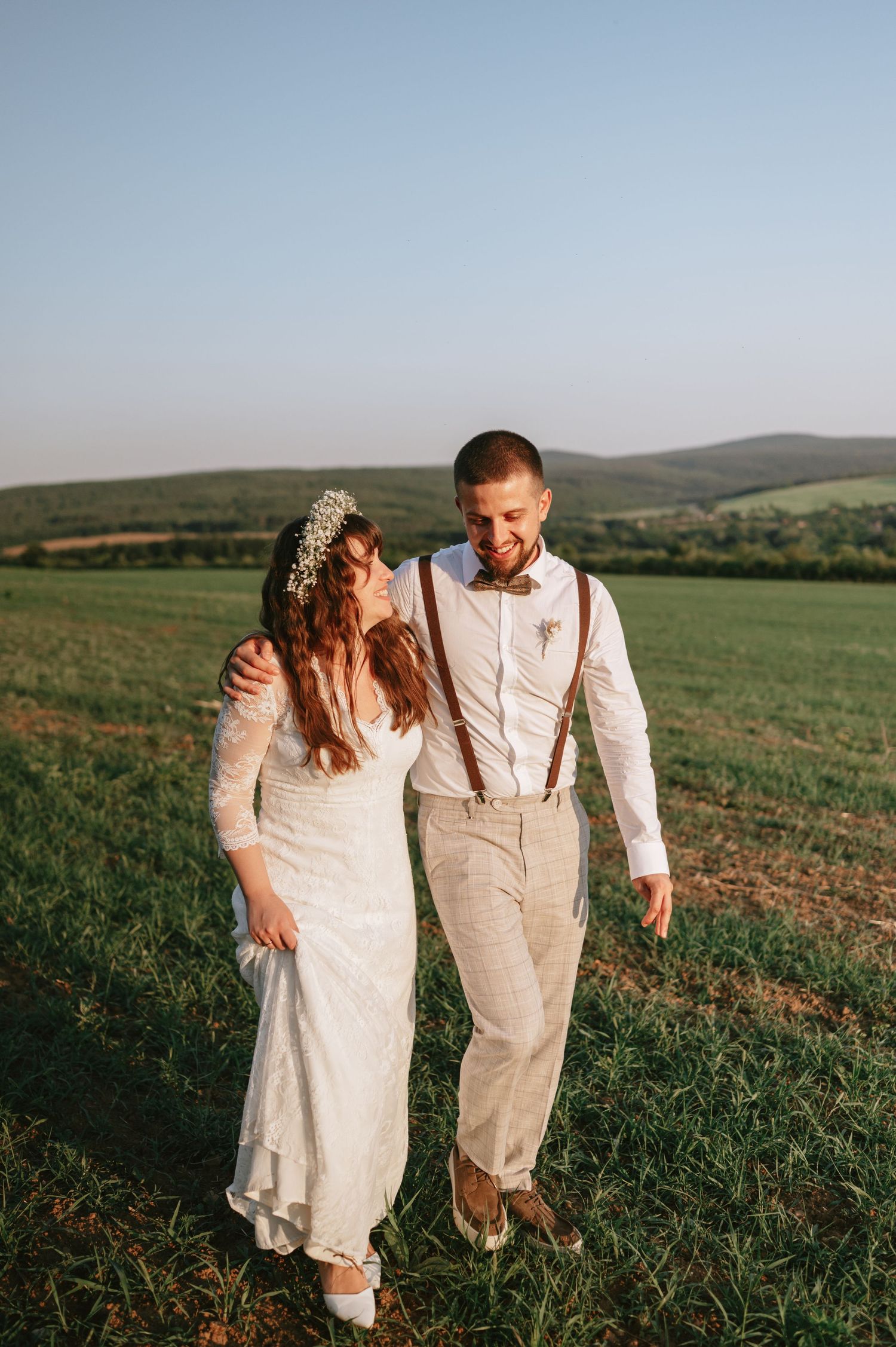 Joyful wedding couple laughing together in a hilltop meadow during sunset.