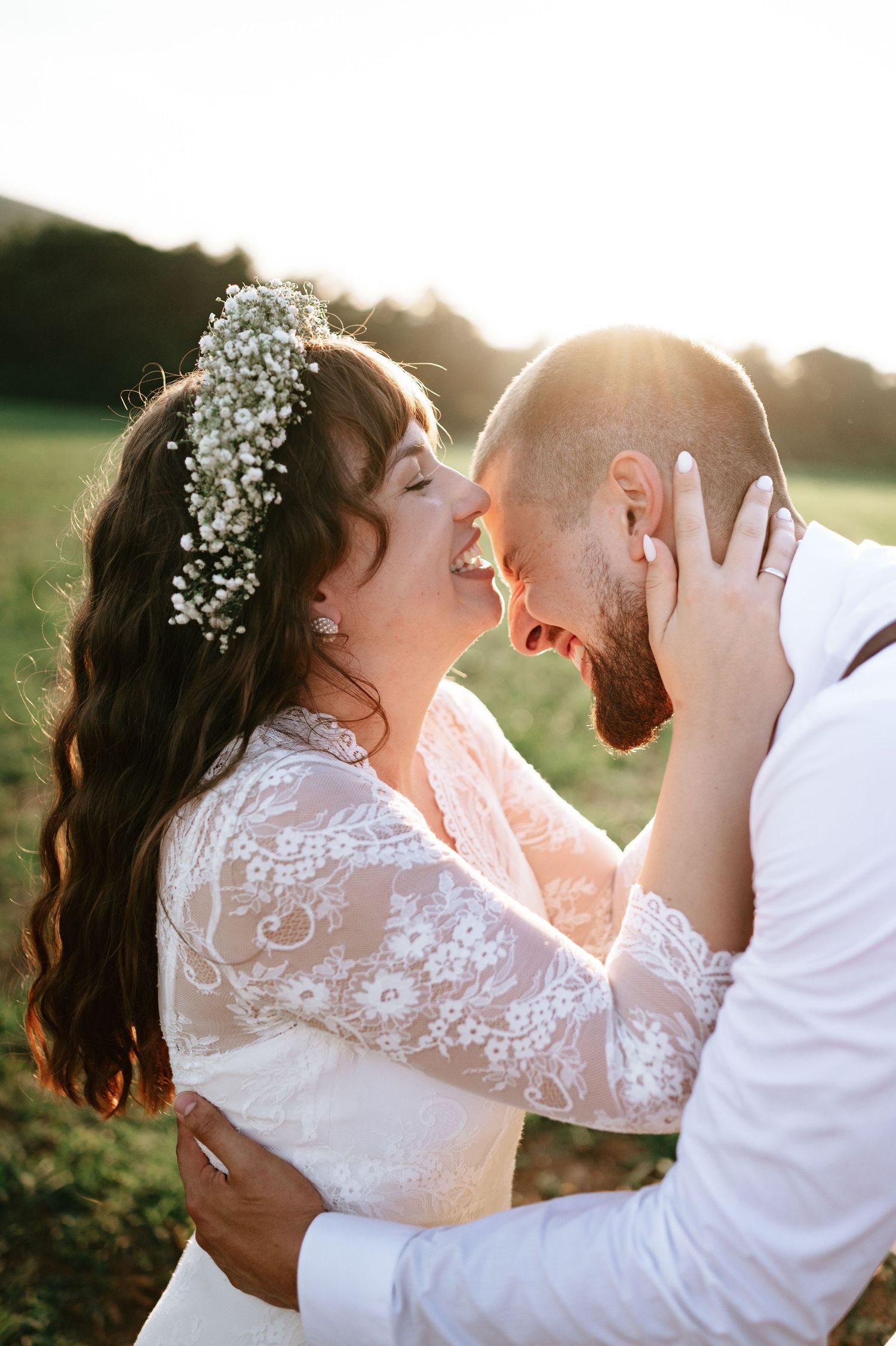 Bride in lace gown and groom share passionate kiss during golden hour wedding photography.