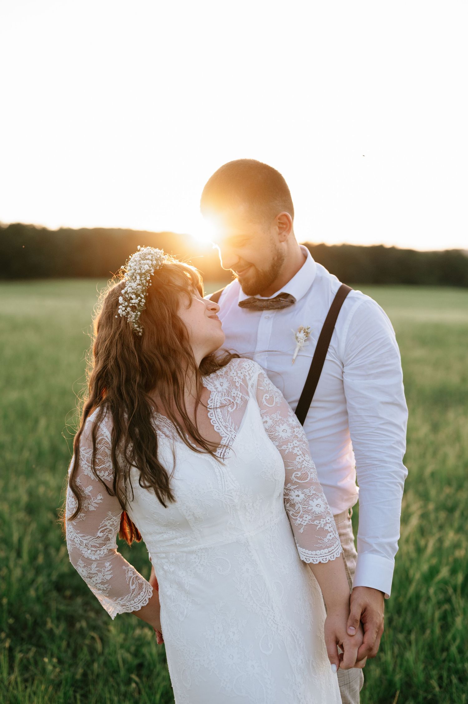 Intimate wedding couple embraces in a sunlit field during golden hour.