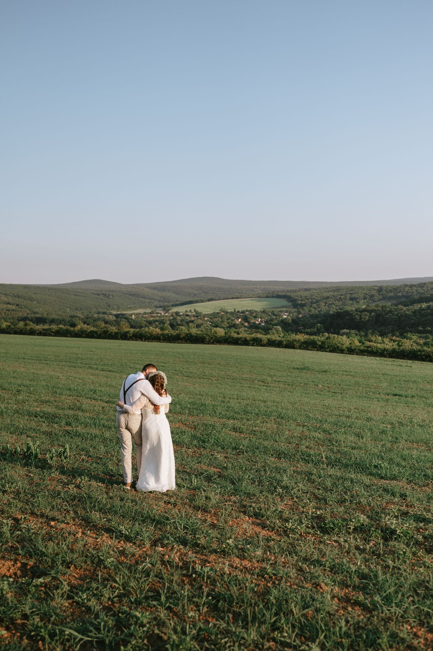 A couple sits together on a grassy hillside overlooking a scenic valley.