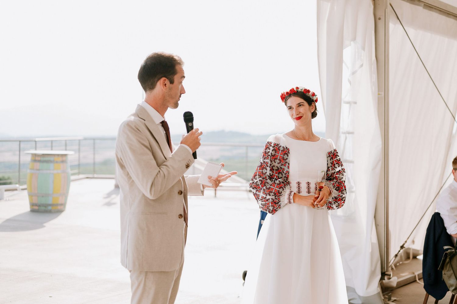 Wedding celebration in a bright white tent venue with guests gathered for speeches.