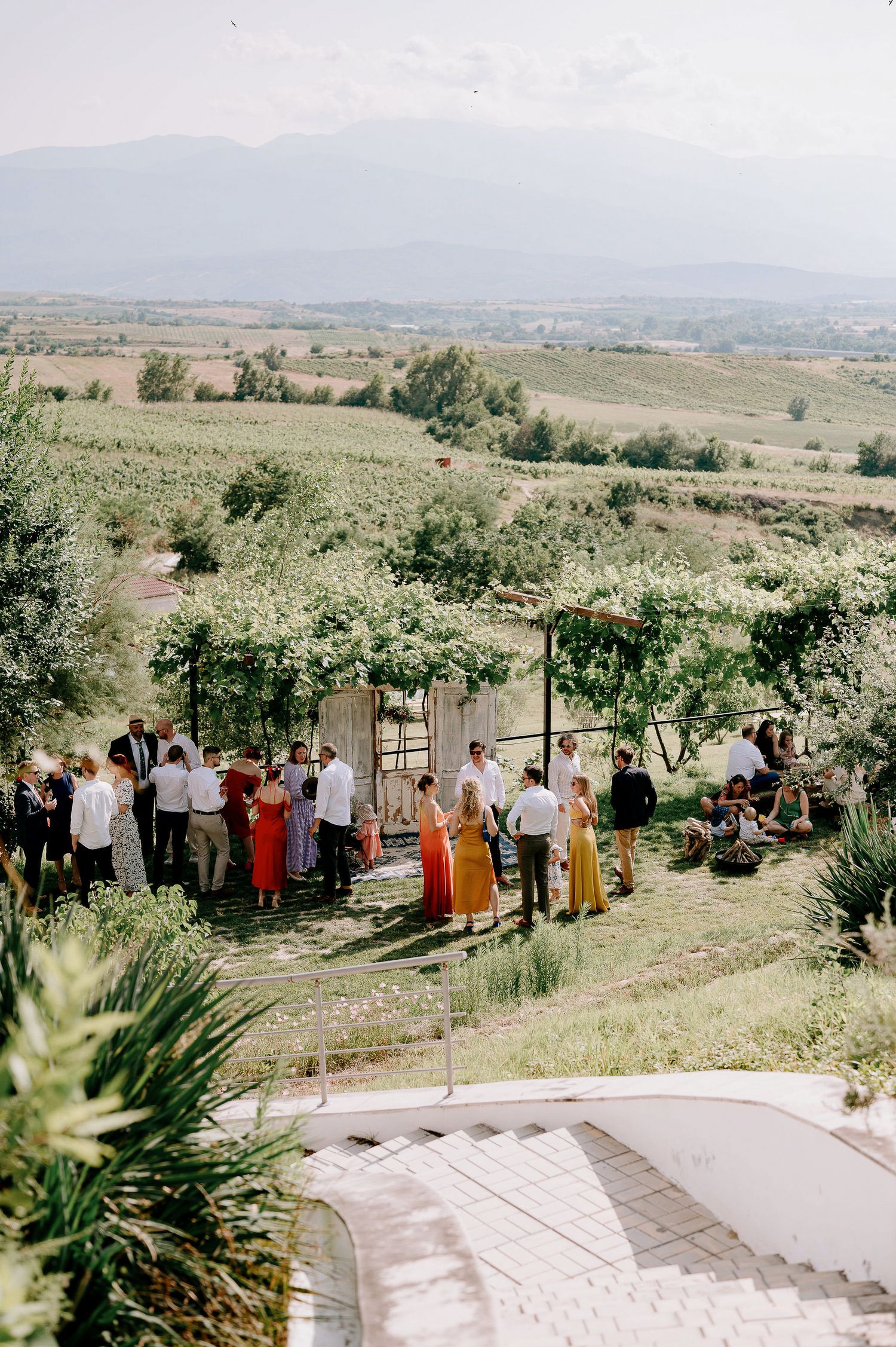 Panoramic view of wedding guests gathered on a scenic hillside under clear skies.