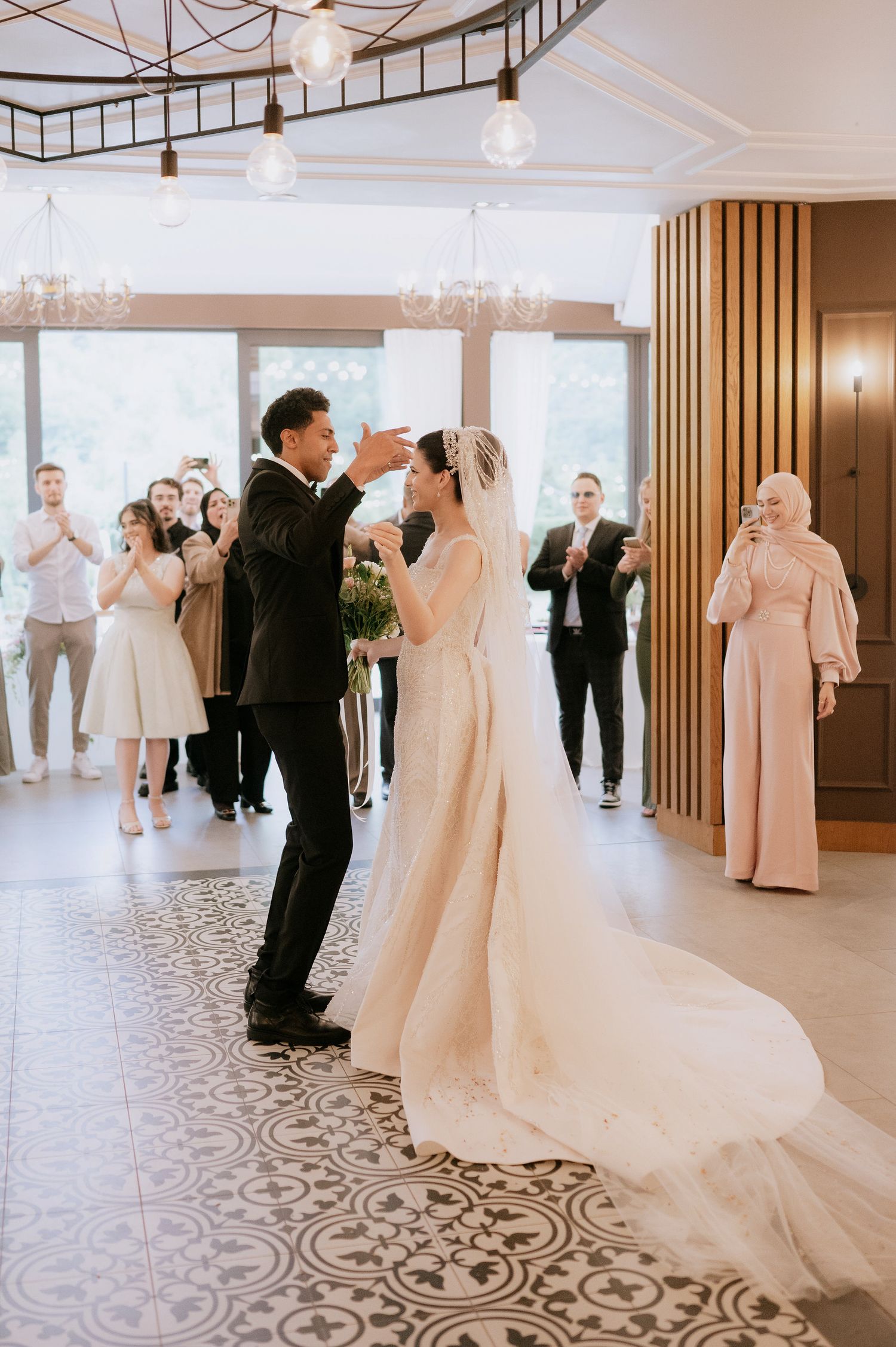 Wedding celebration in a modern venue featuring elegant chandeliers and patterned tile floors.