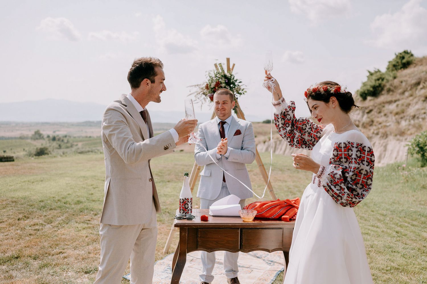 Desert wedding ceremony with rustic decor and red floral accents against rolling hills.