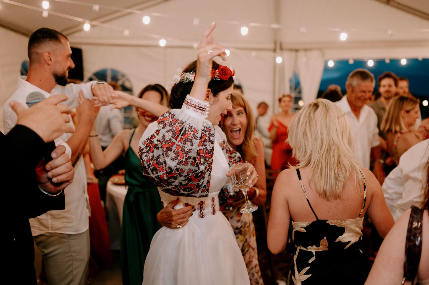Wedding party dancing and celebrating in a white tent venue with string lighting.