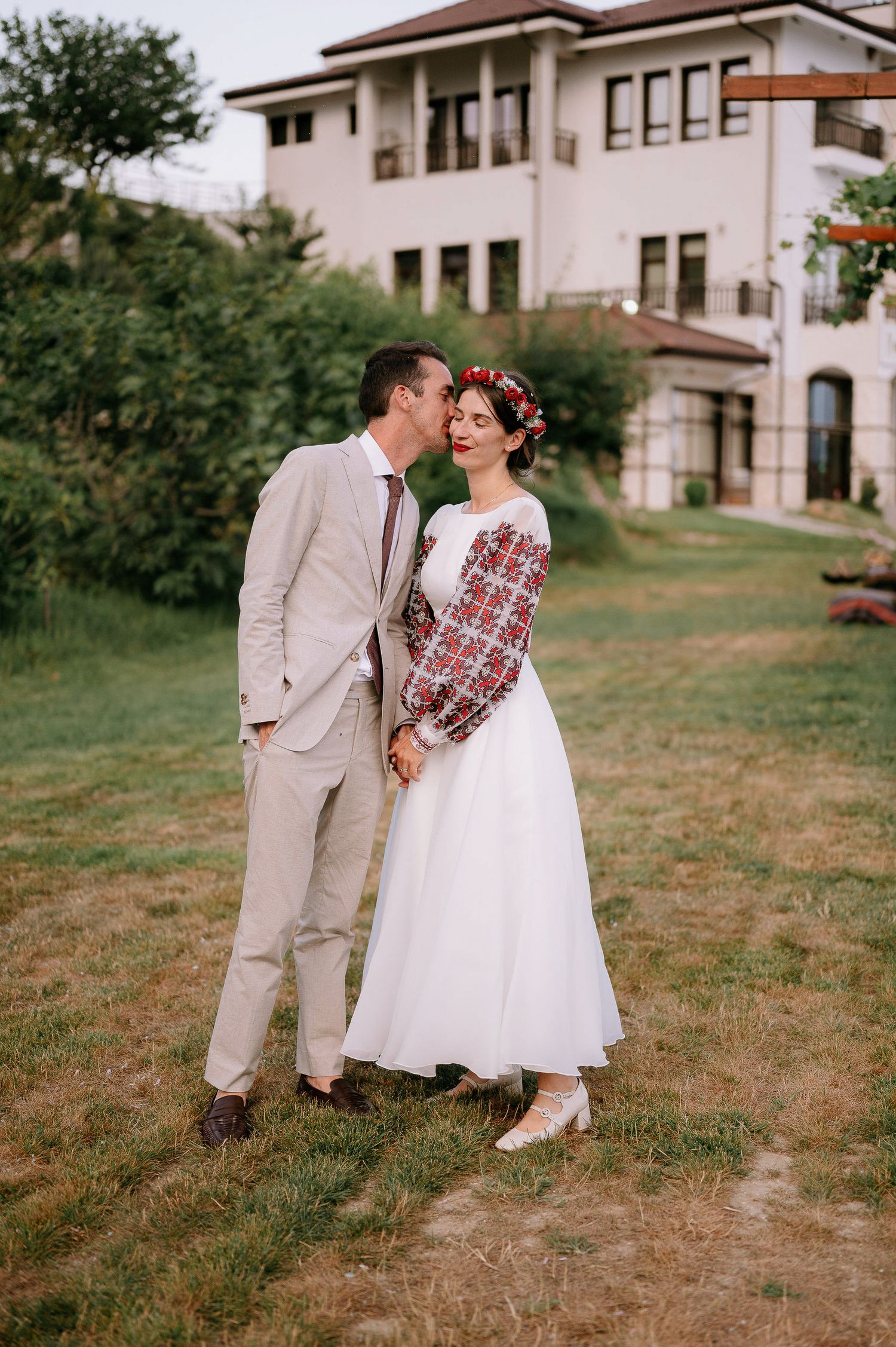 A romantic wedding moment captured outdoors with a couple in vintage-inspired dress and suit.