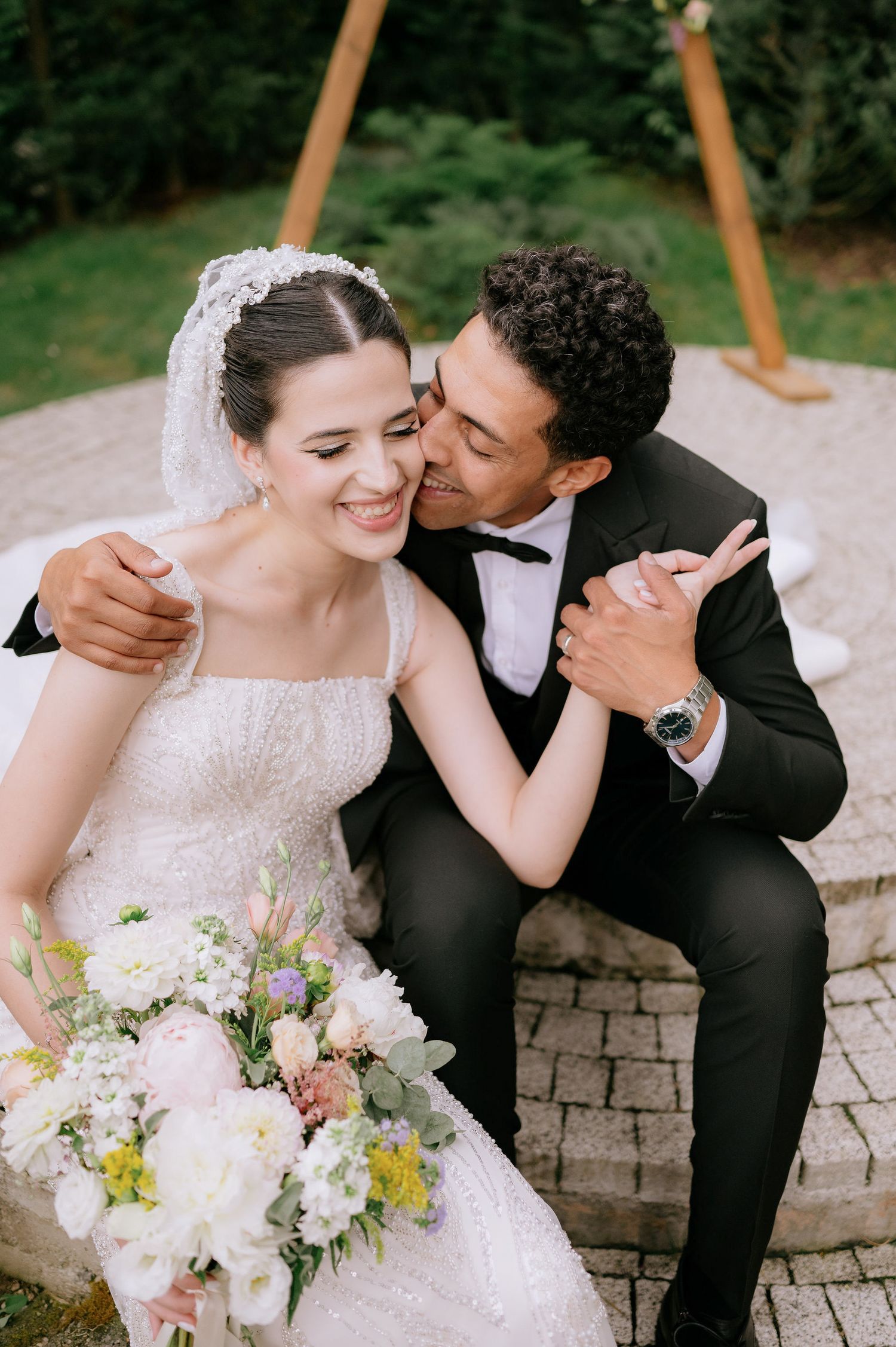 Romantic wedding couple sharing tender moment with white floral bouquet.