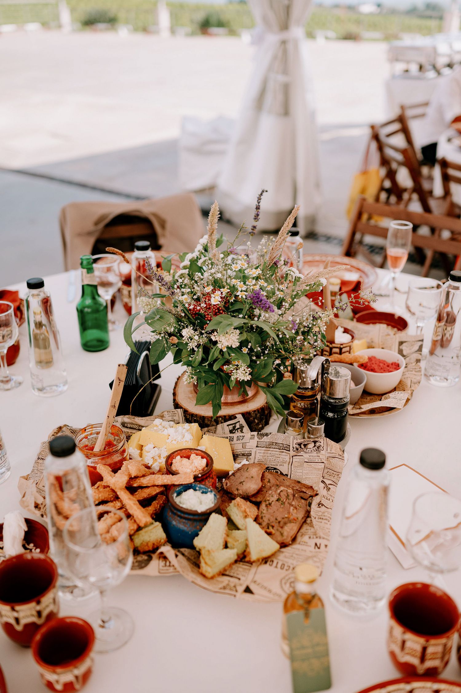 Wedding reception table with charcuterie board, floral centerpiece, and wine glasses in natural lighting.